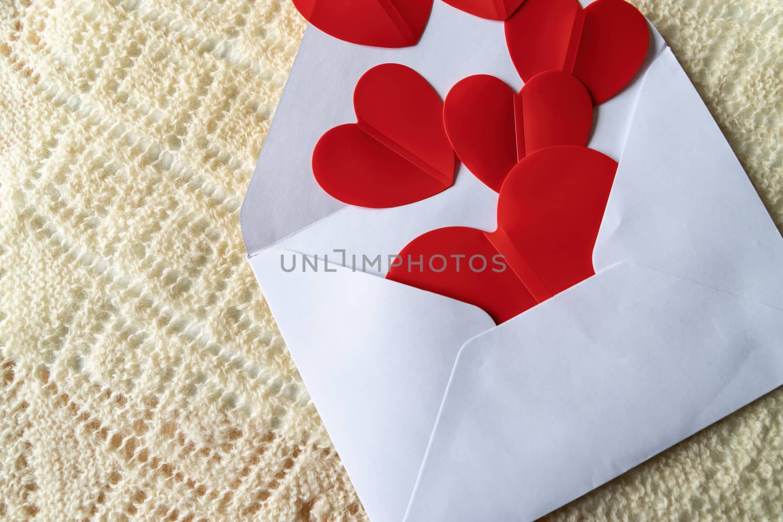 Red hearts and a white mail envelope on a background of knitted texture. Love heart frame. Happy mother's day concept. Love symbol. Holiday card background, copy space for text.