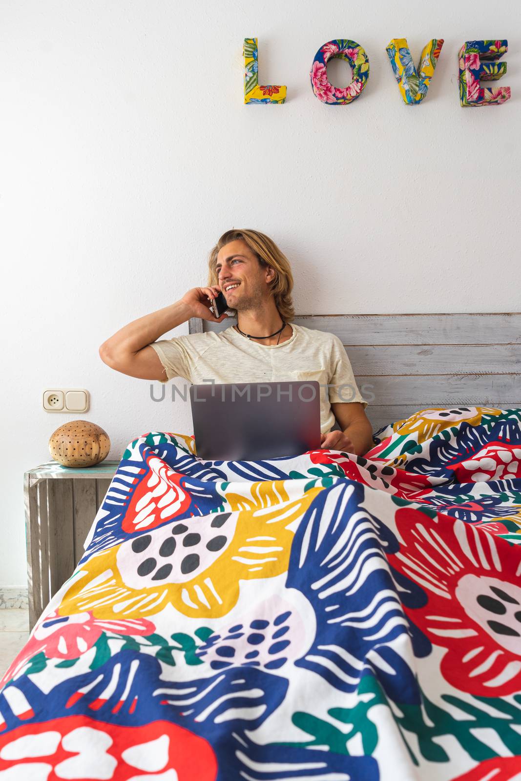 Young man with medium long blonde hair, with a beard and mustache working on the computer from home during quarantine, from bed. Talking to a coworker. Concept adapted to the new reality.