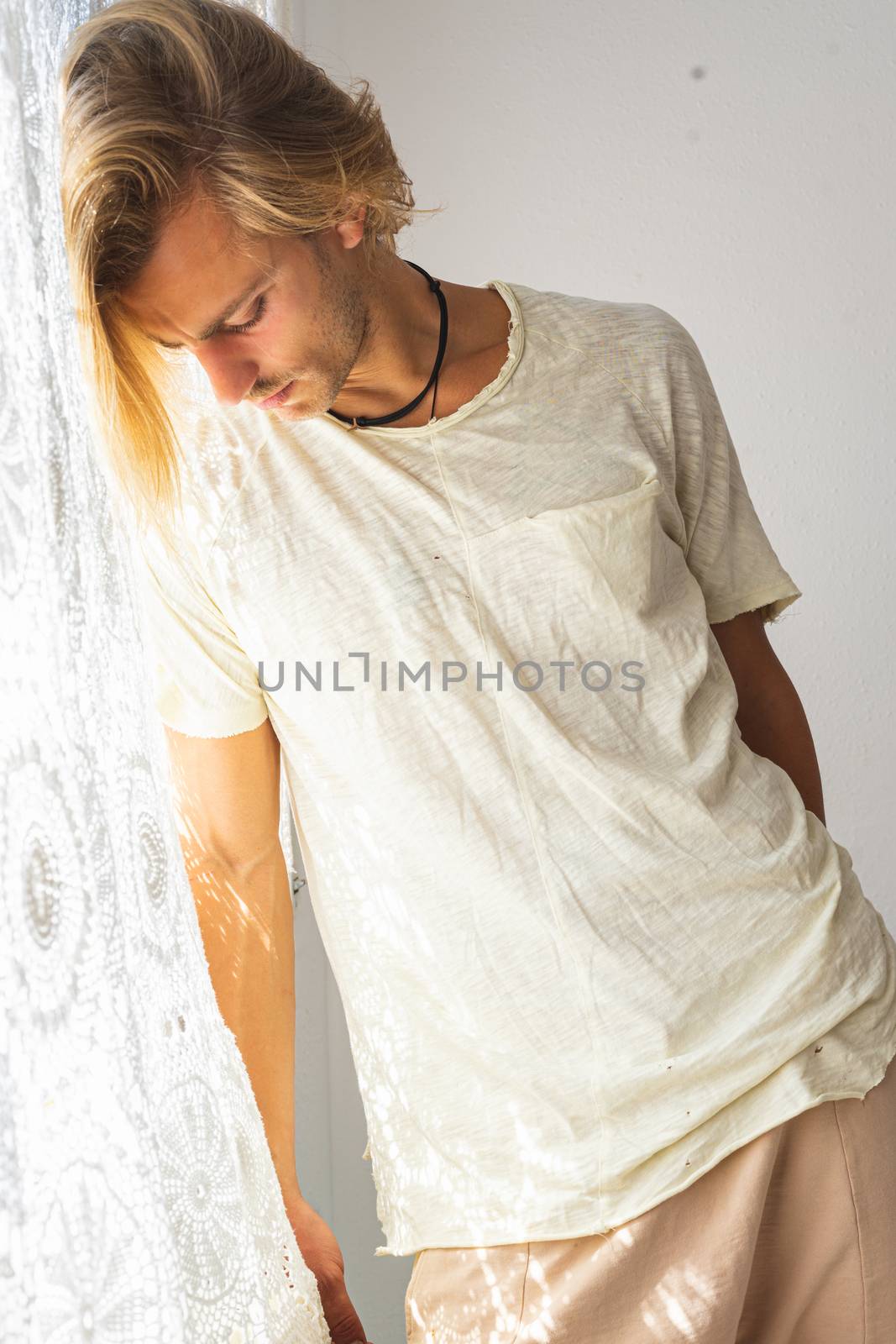 Young man with medium long blonde hair frustrated at not being able to leave home. Looking down on a white background. Loneliness and silence concept.