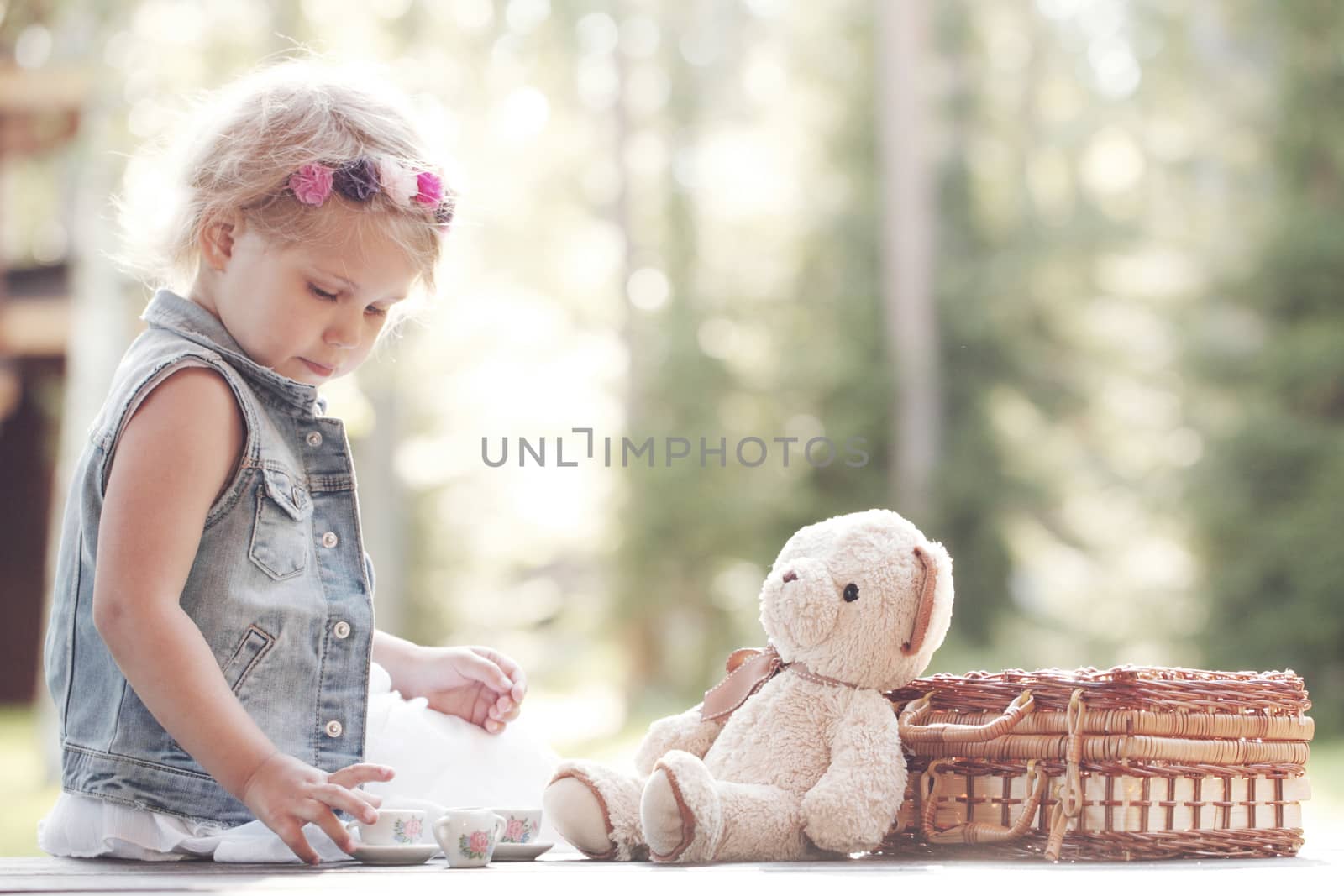 Pretty girl playing with teddy bear outdoors drinking tea