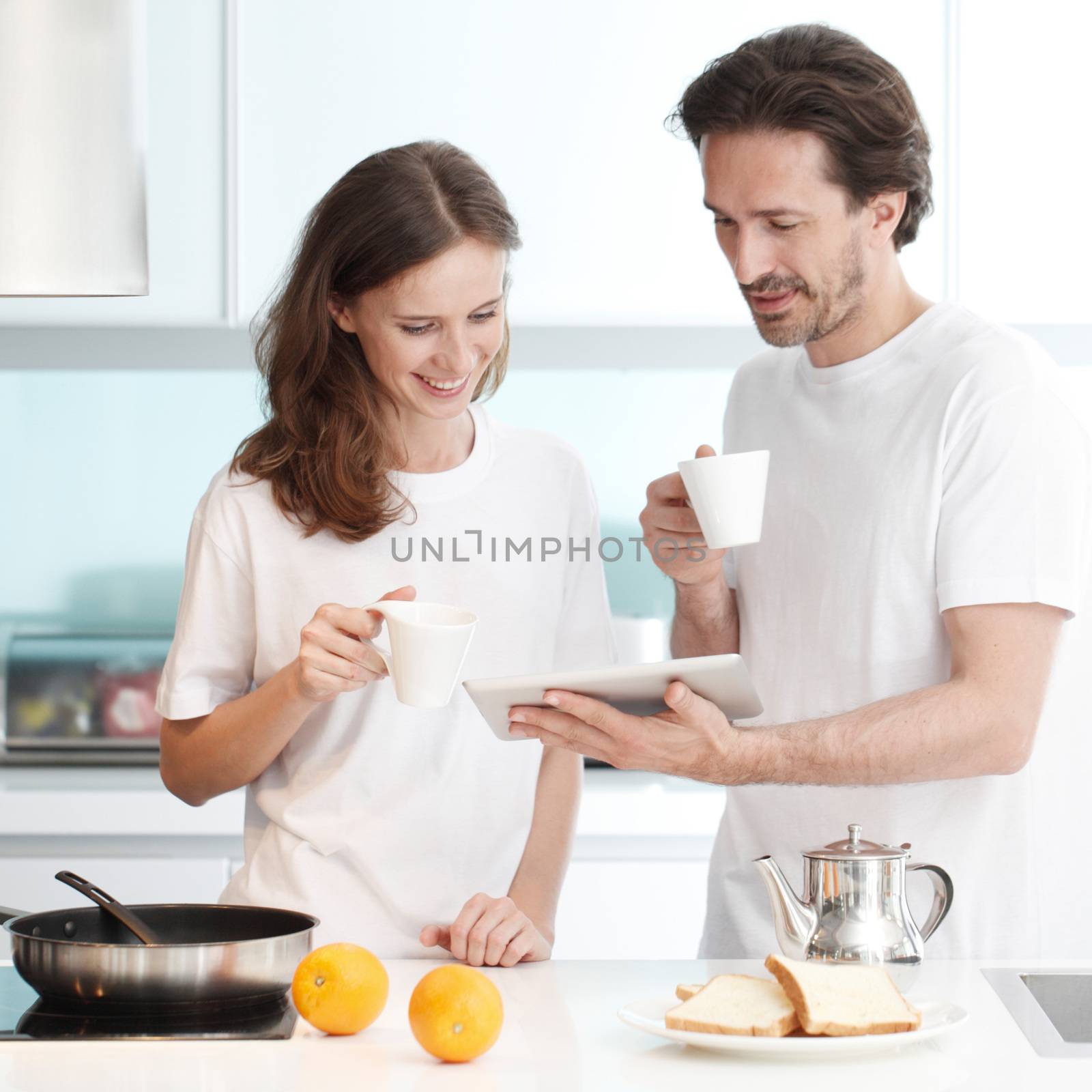 Couple cooking breakfast together in kitchen using tablet pc