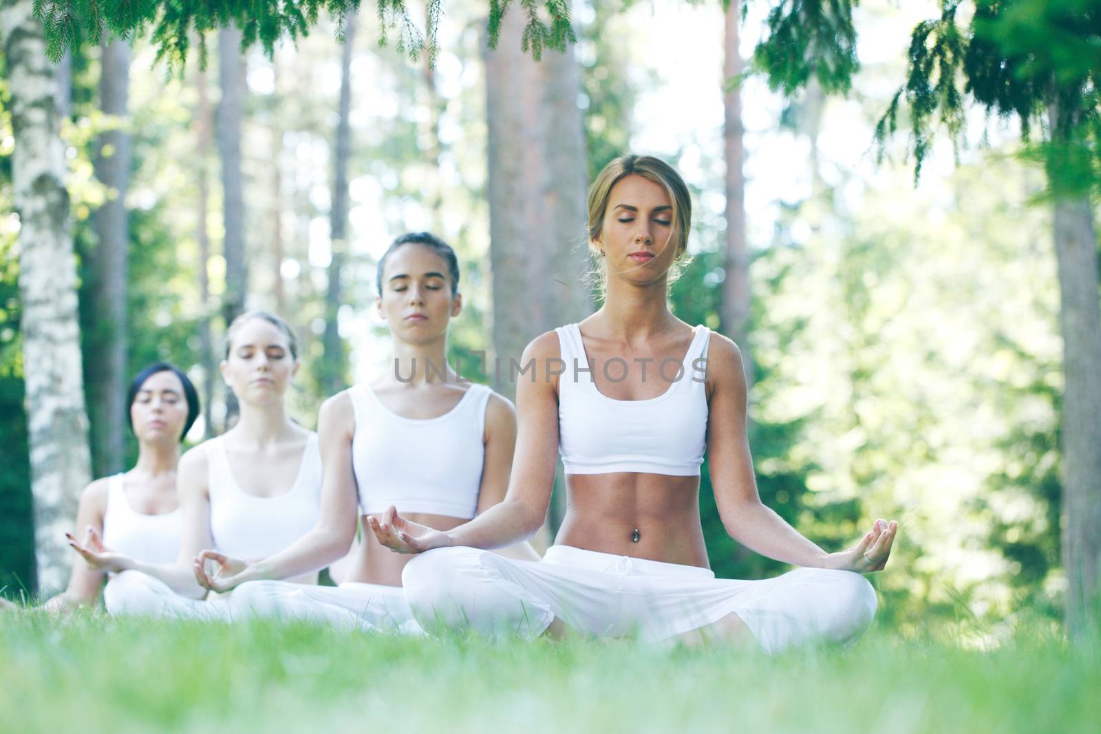 Women in white sportswear sitting in lotus position during group yoga training at park