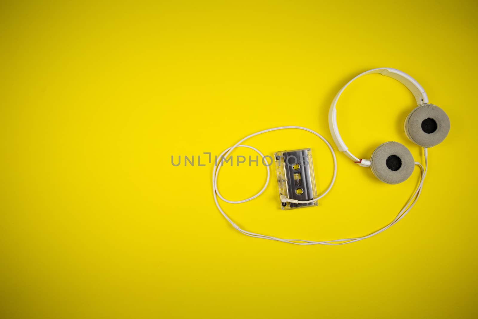 Audio cassette tape and modern headphones on a yellow background, music