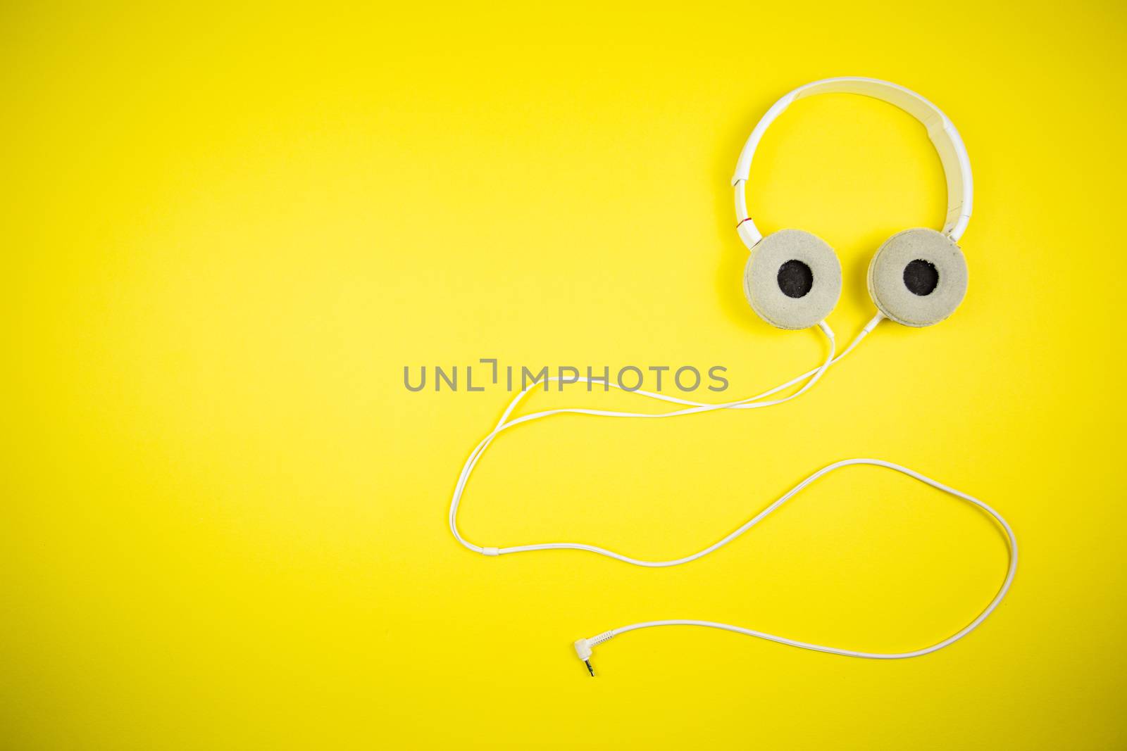 White audio headphones with a 3.5 mm wire on a yellow background, music