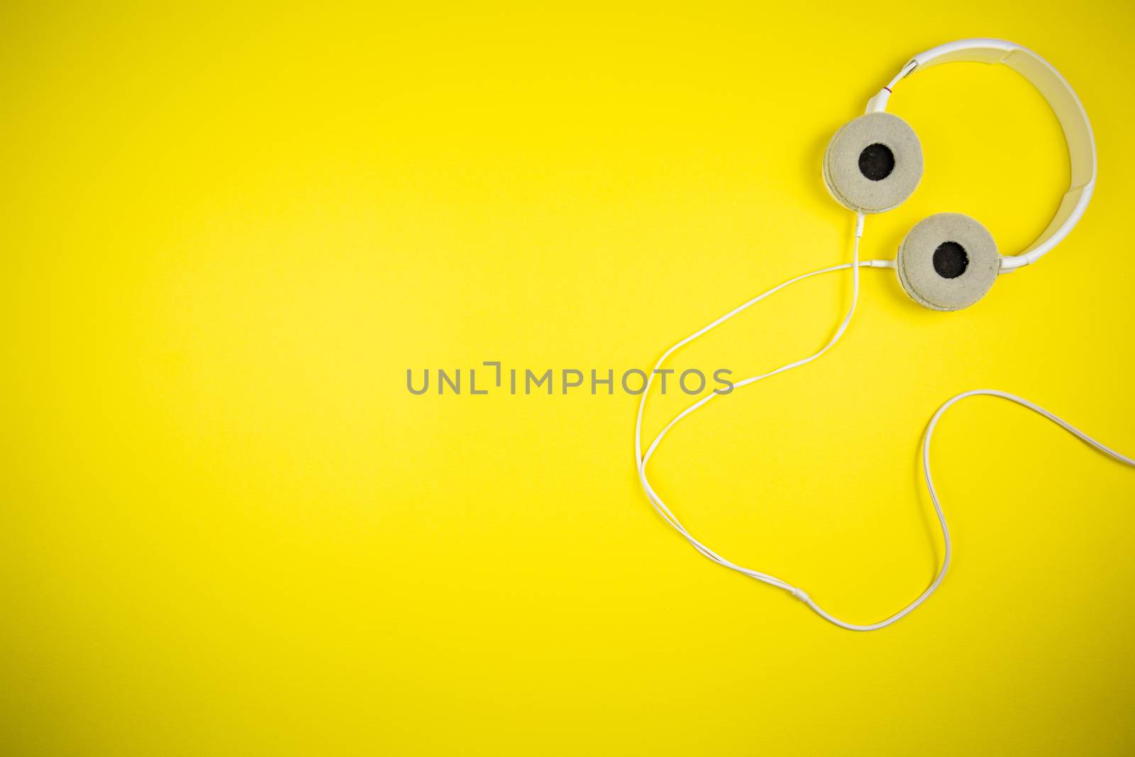 White audio headphones with a 3.5 mm wire on a yellow background, music