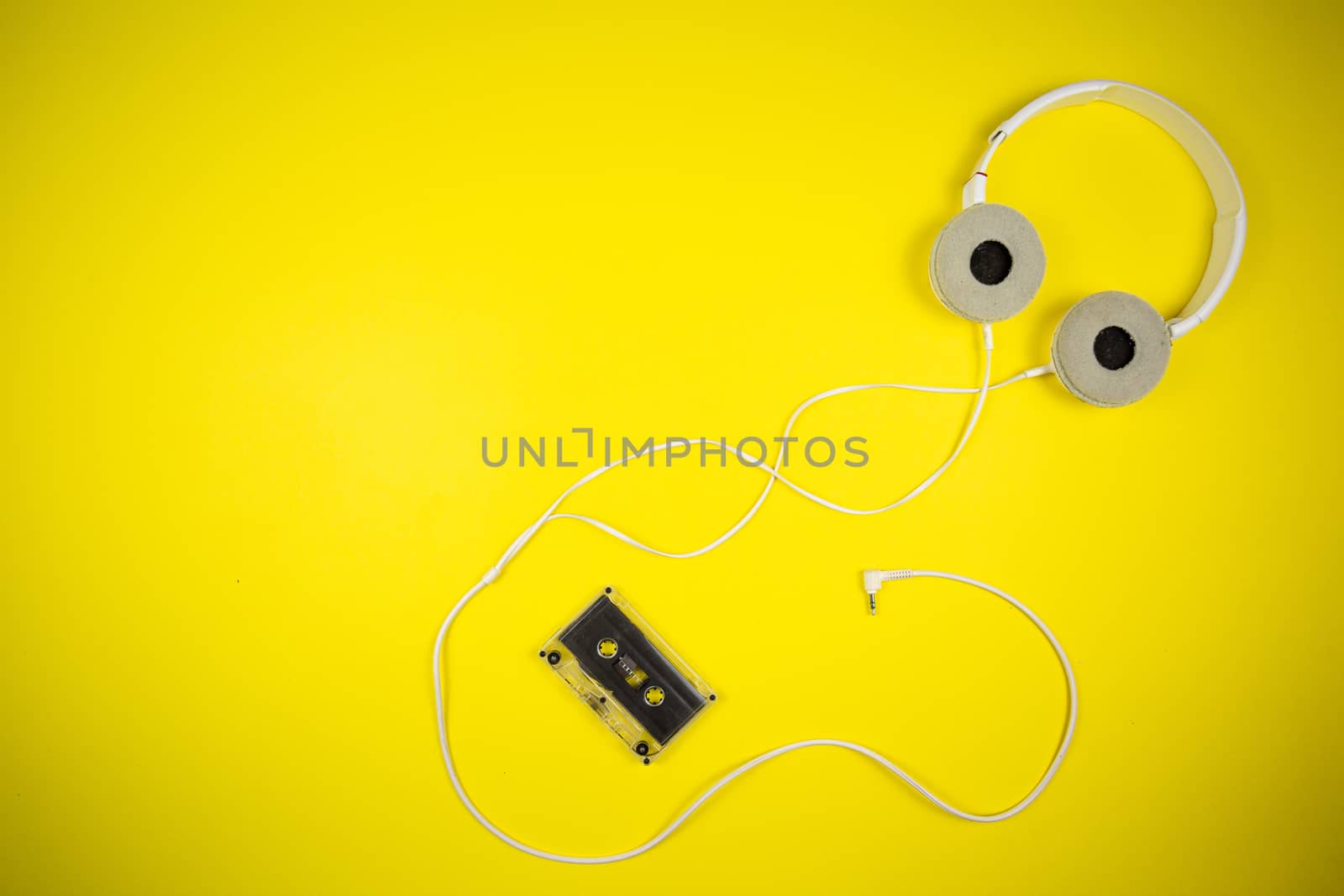 Audio cassette tape and modern headphones on a yellow background, music