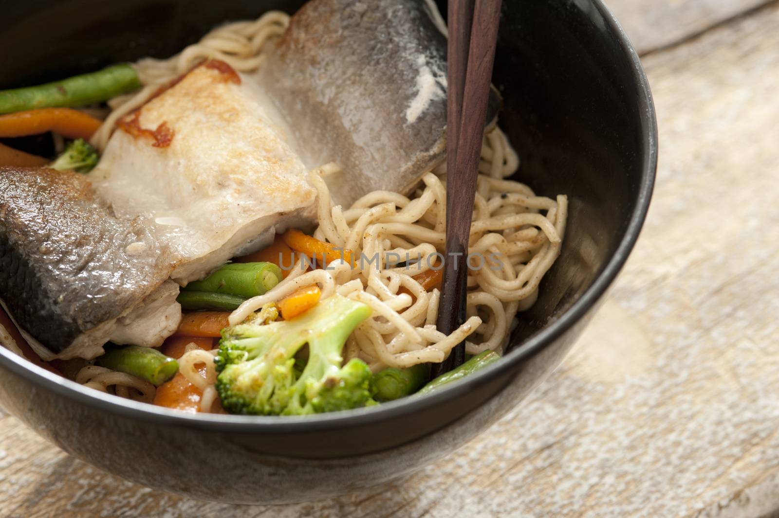 Healthy Asian vermicelli noodles with fish and fresh boiled broccoli and carrots served in a black bowl