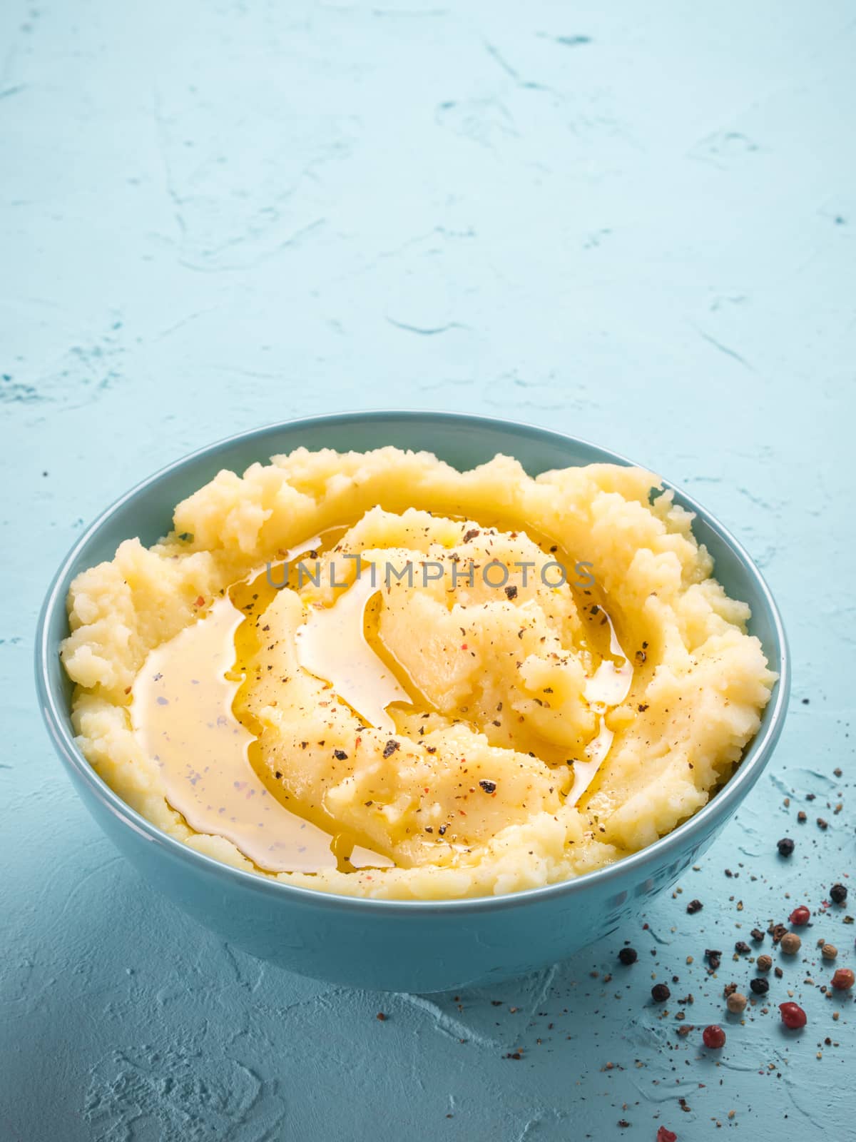 Mashed potatoes with peppers and olive oil in blue bowl on blue concrete background. Vertical.