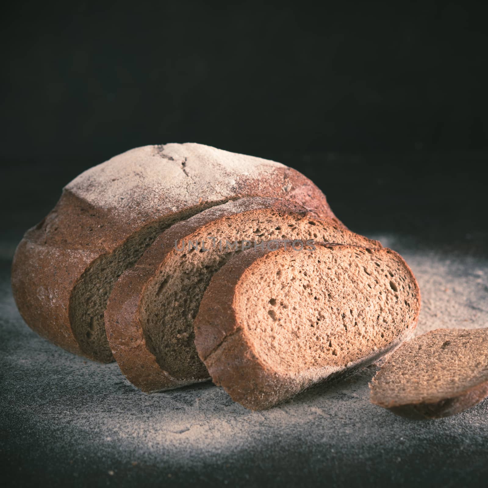 Sliced homemade sourdough rye bread with rye flour on black textured background. Copy space. Low key Toned image