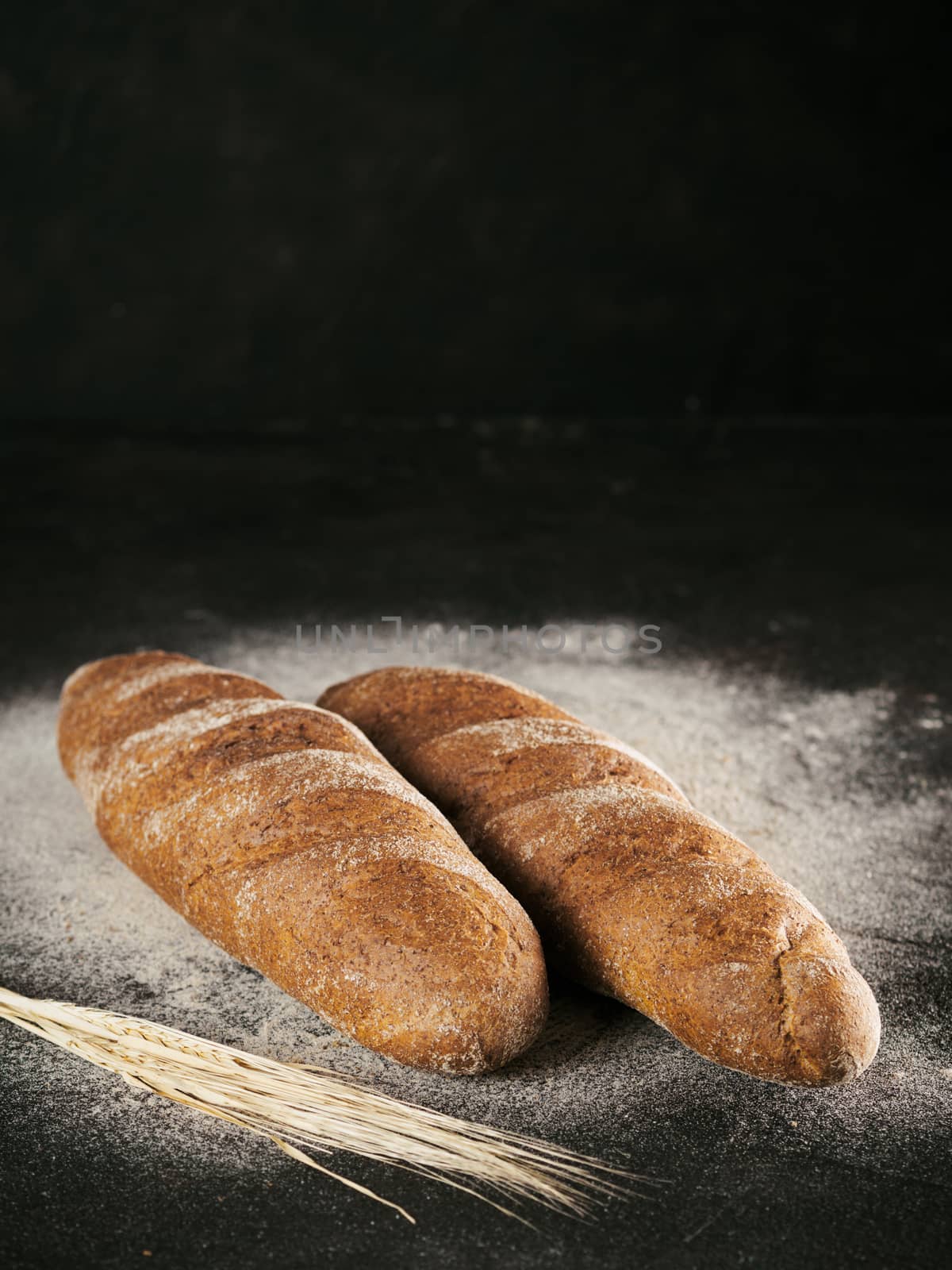 Two whole homemade rye loaf bread with buckwheat flour on black textured background. Copy space. Low key