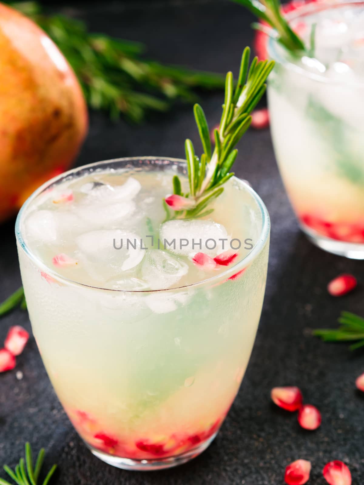 Autumn and winter cocktails idea - white sangria with rosemary, pomegrante and lemon juice and ingredients on black cement background.