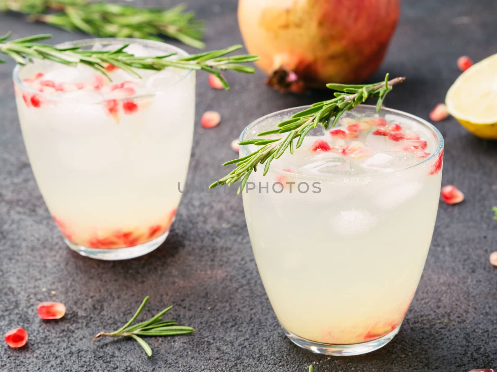 Autumn and winter cocktails idea - white sangria with rosemary, pomegrante and lemon juice and ingredients on black cement background.