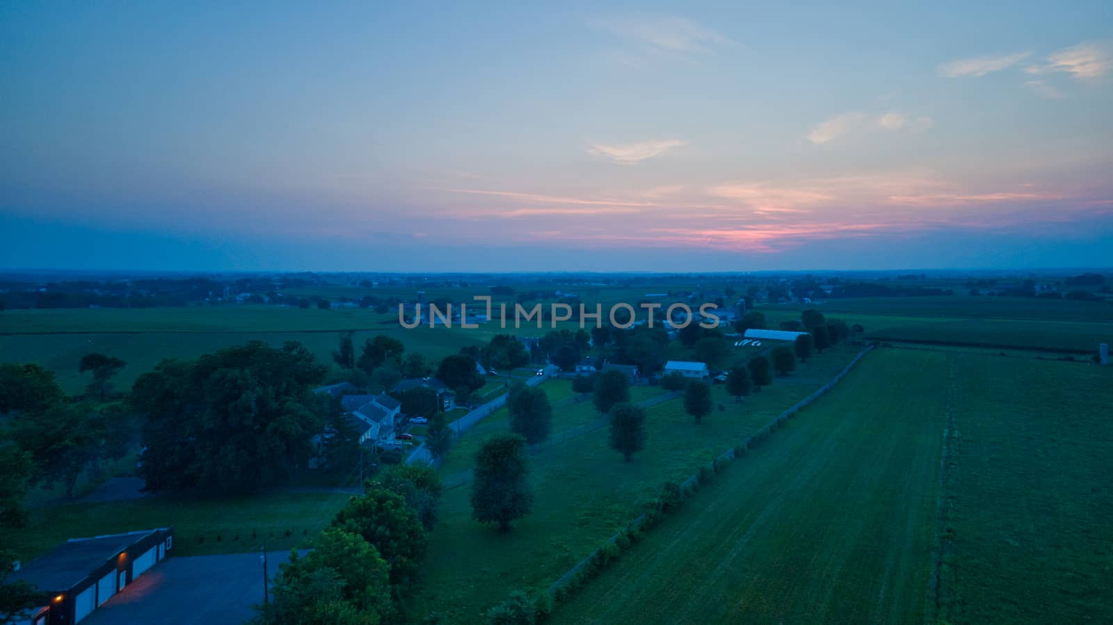 Aerial view of a summer sunset over farm lands with blue skies and red sun