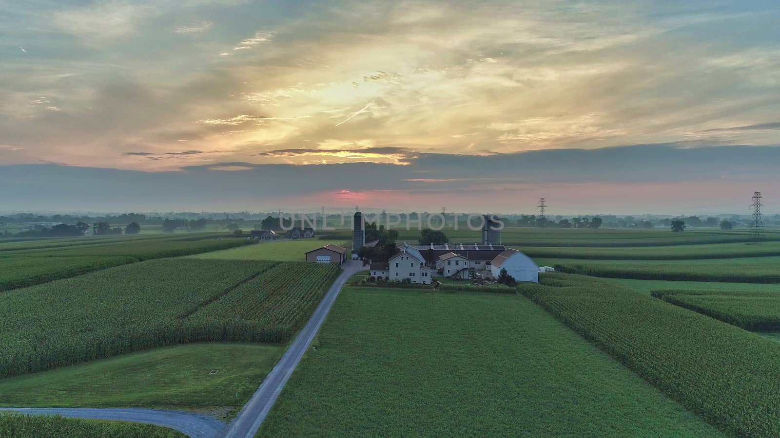 Aerial view of a summer sunset over farm lands with blue skies and red sun