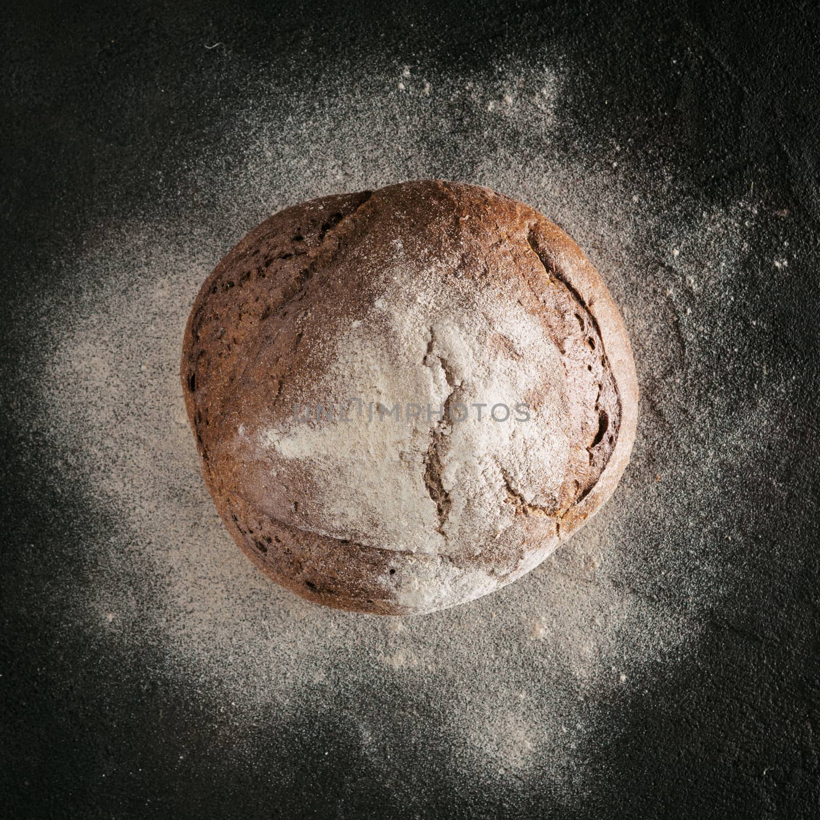 Whole homemade rye bread with rye flour on black textured background. Top view or flat-lay. Low key