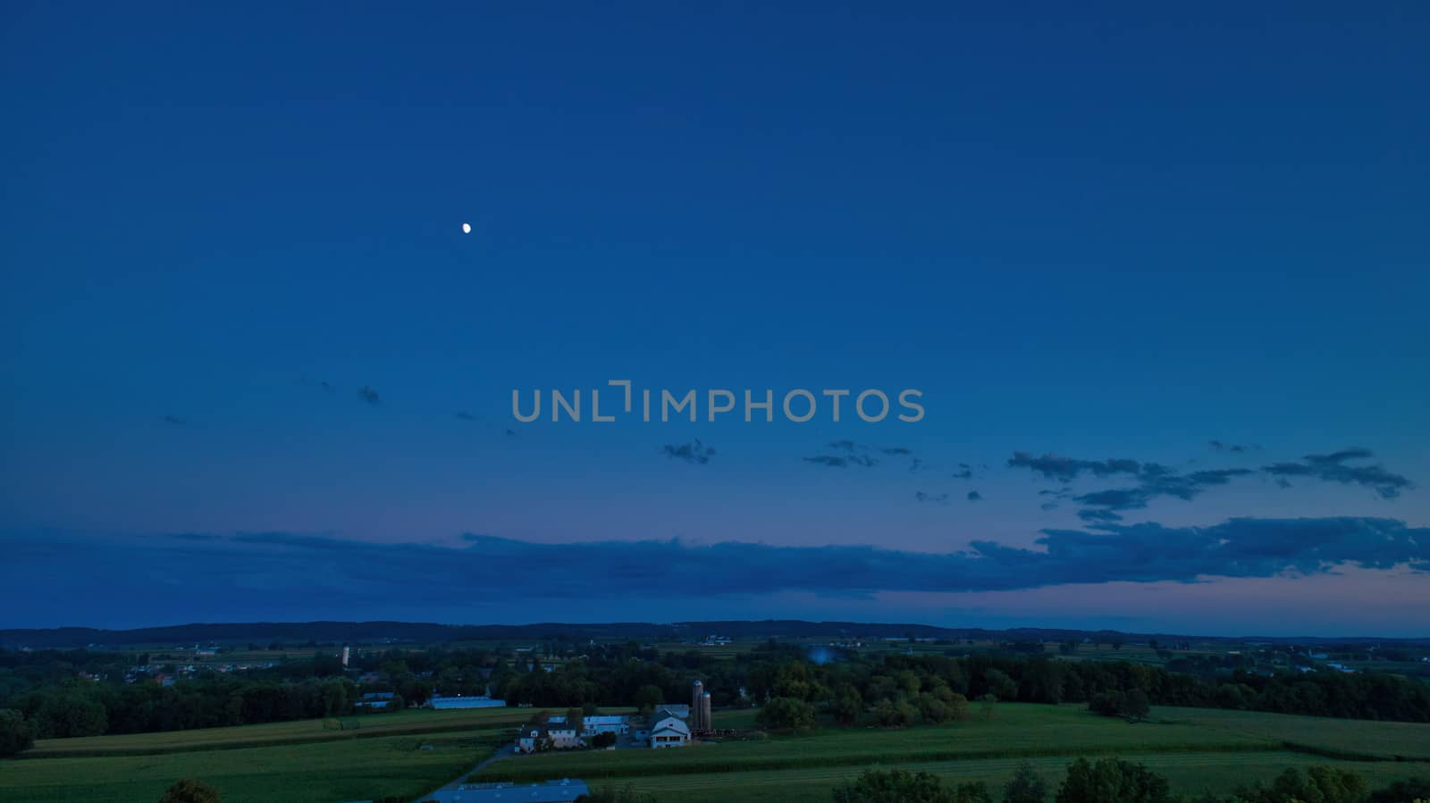 Sunset over barns, silos and green farmlands with blue, red and orange skies and a few clouds