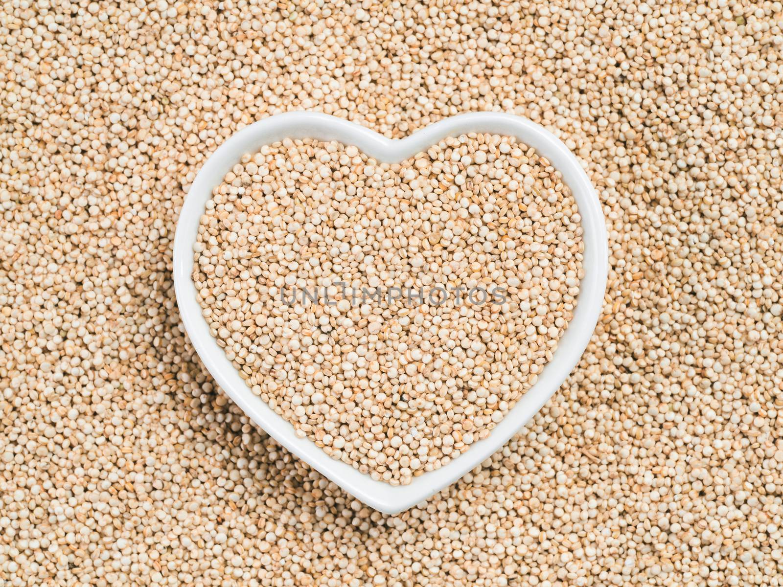 Quinoa in heart-shaped bowl on quinoa background. Gluten free ancient grain for healthy diet. I love quinoa concept. Copy space.