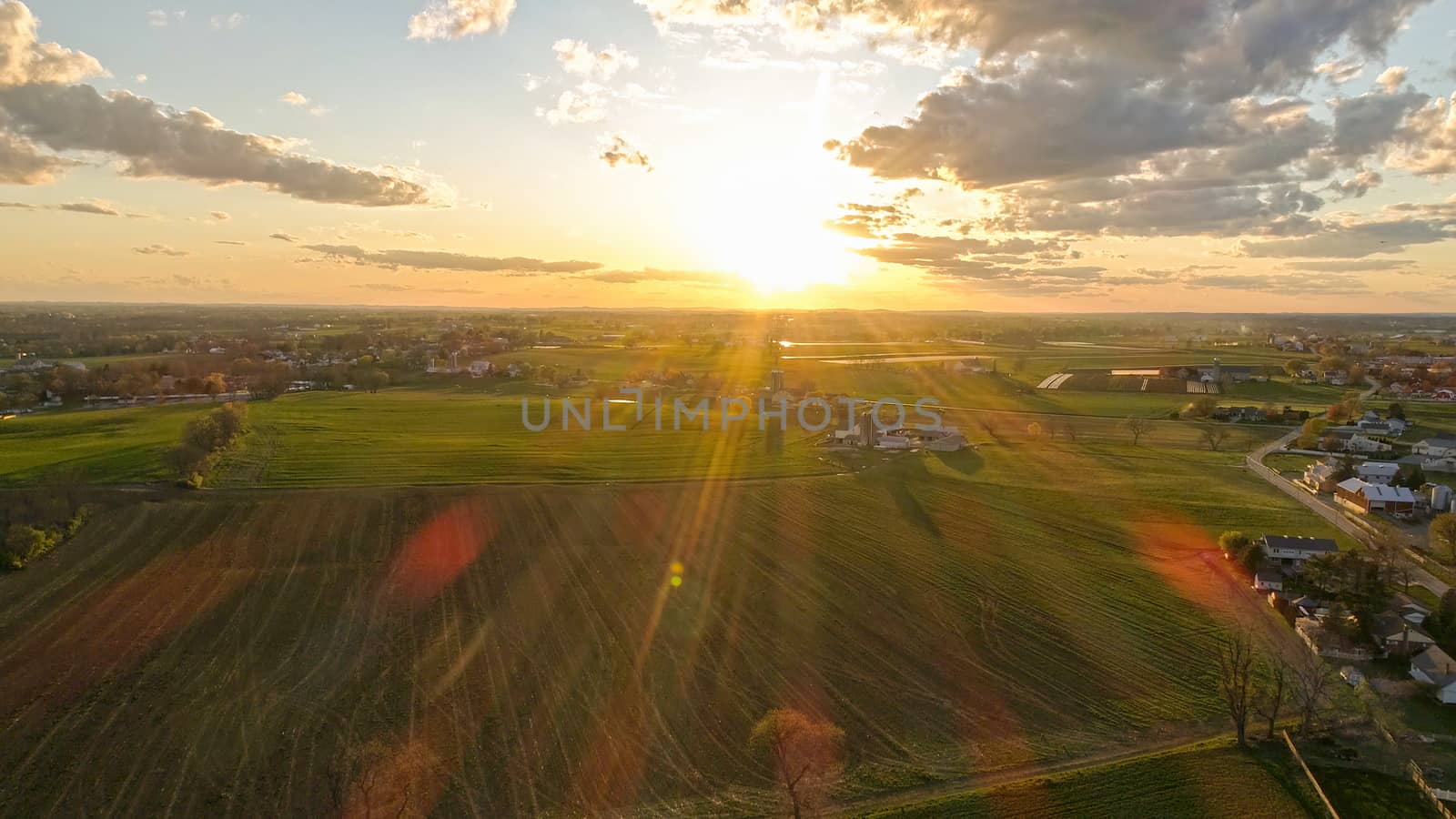Aerial view of a Sunset over barns, silos and farmlands during the golden hour with blue sky, clouds and red sun