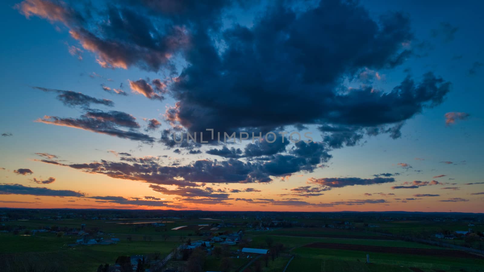 Aerial view of a Sunset over barns, silos and farmlands during the golden hour with blue sky, clouds and red sun