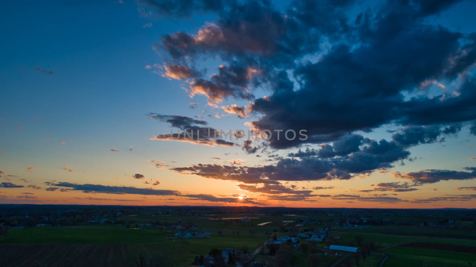 Aerial view of a Sunset over barns, silos and farmlands during the golden hour with blue sky, clouds and red sun