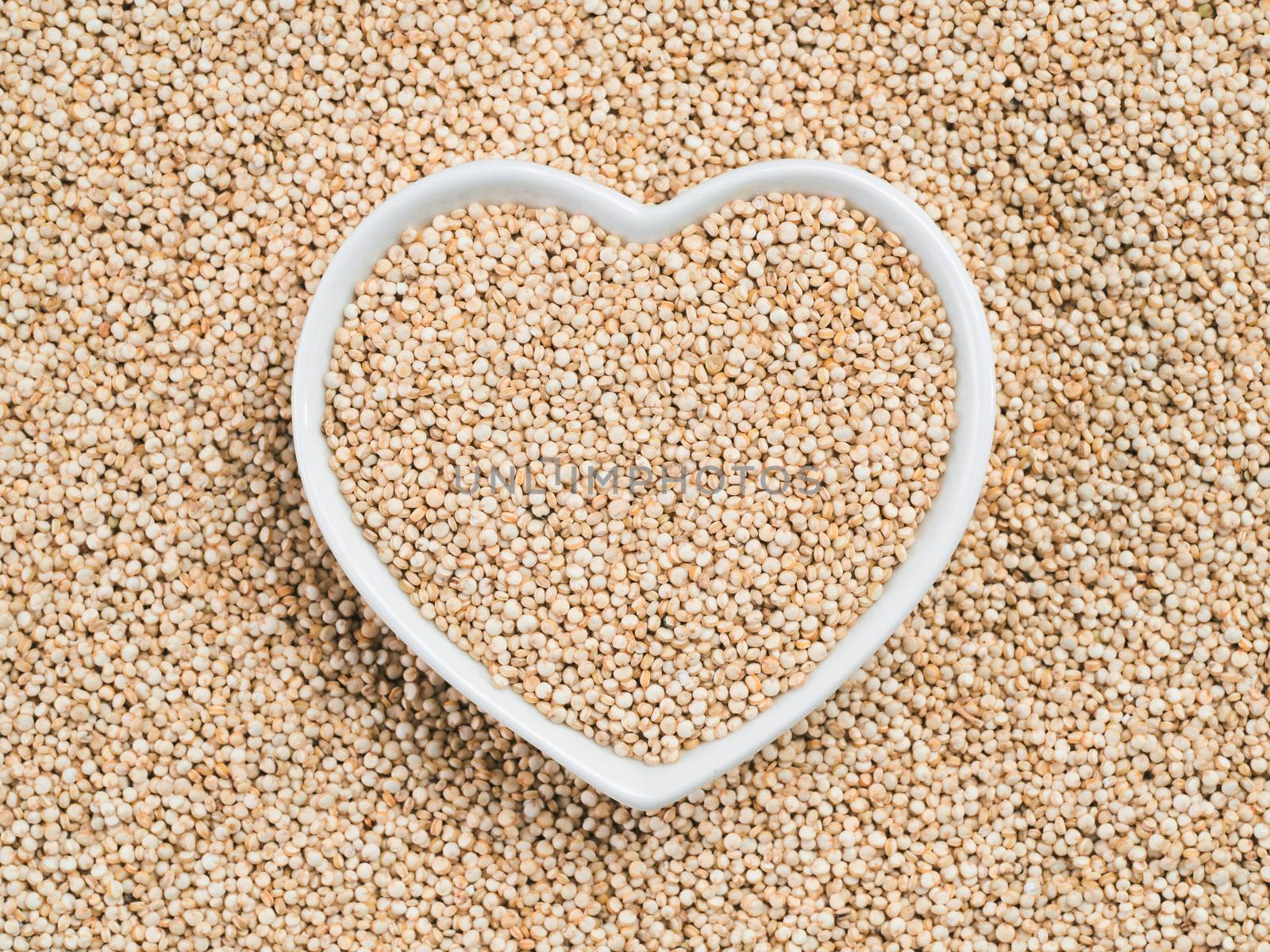 Quinoa in heart-shaped bowl on quinoa background. Gluten free ancient grain for healthy diet. I love quinoa concept. Copy space.