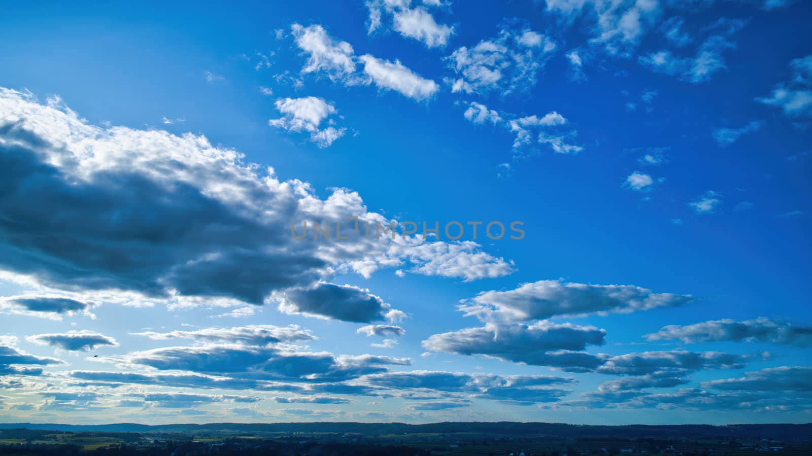 Blue sky and multiple clouds background showing a horizon and a hidden sun