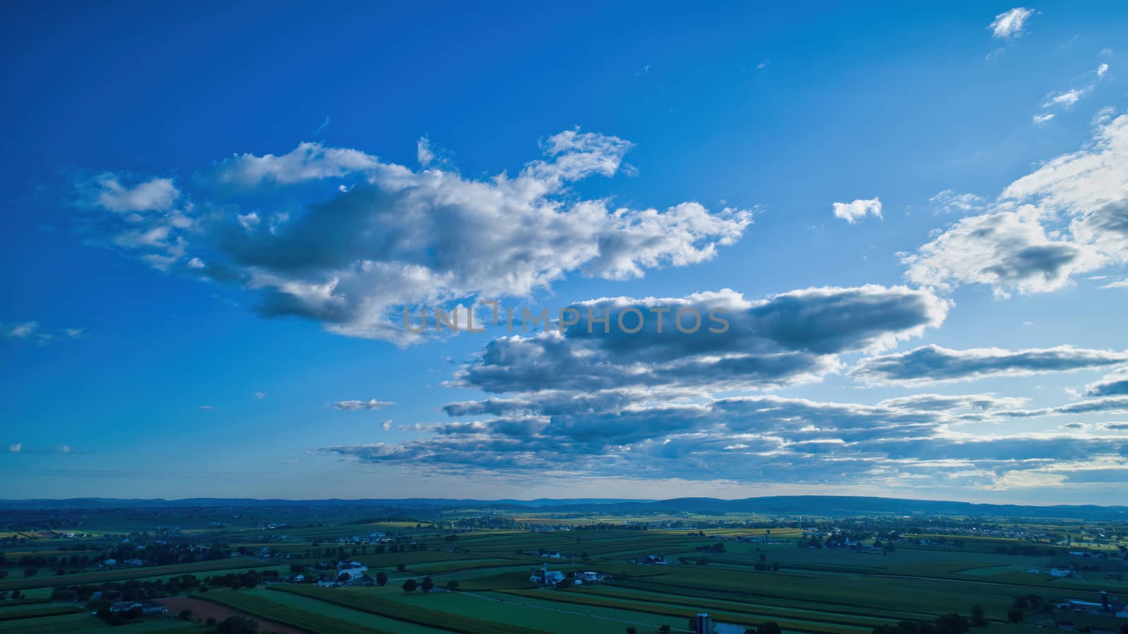 Blue sky and multiple clouds background showing a horizon and a hidden sun