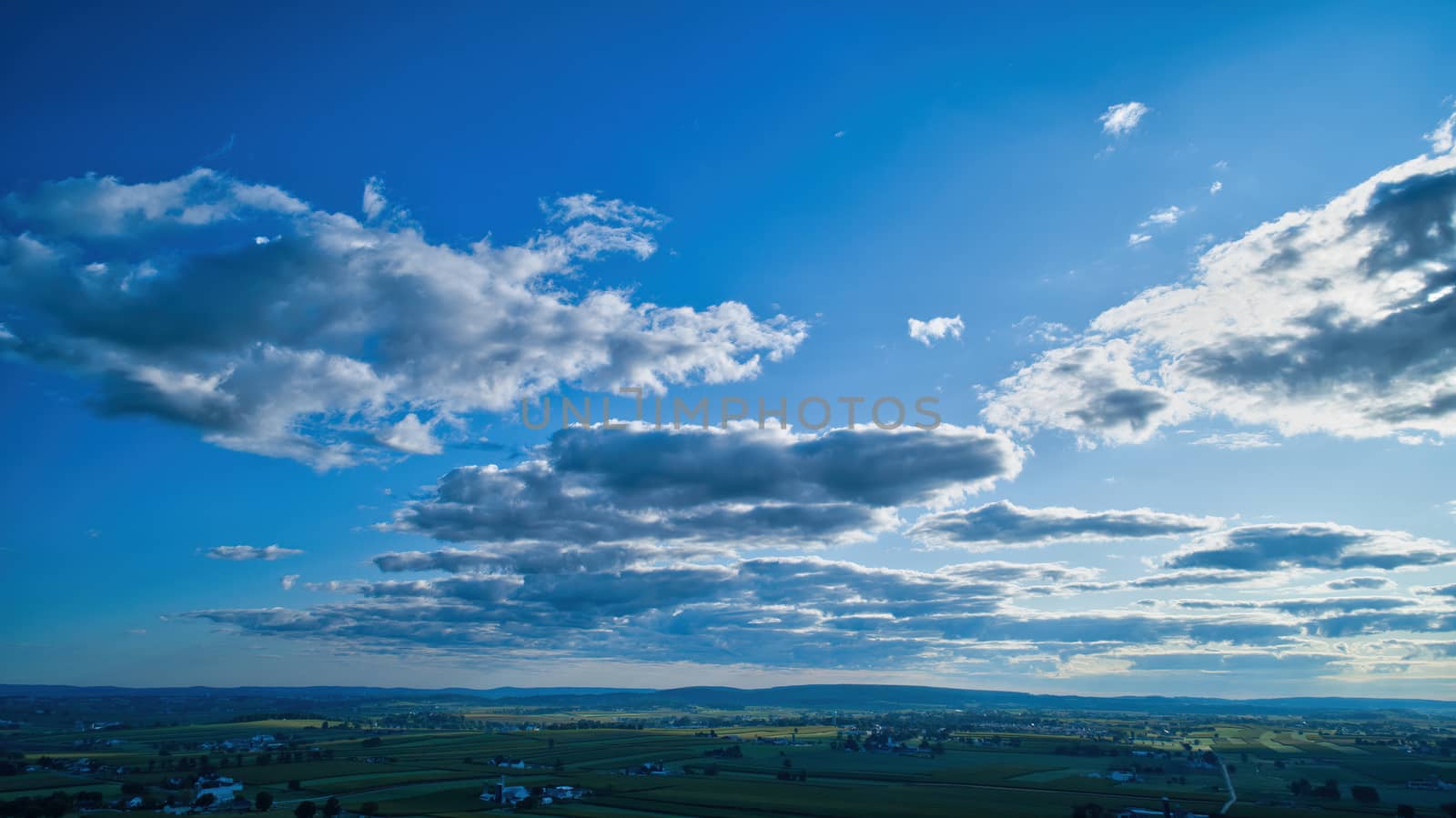 Blue sky and multiple clouds background showing a horizon and a hidden sun