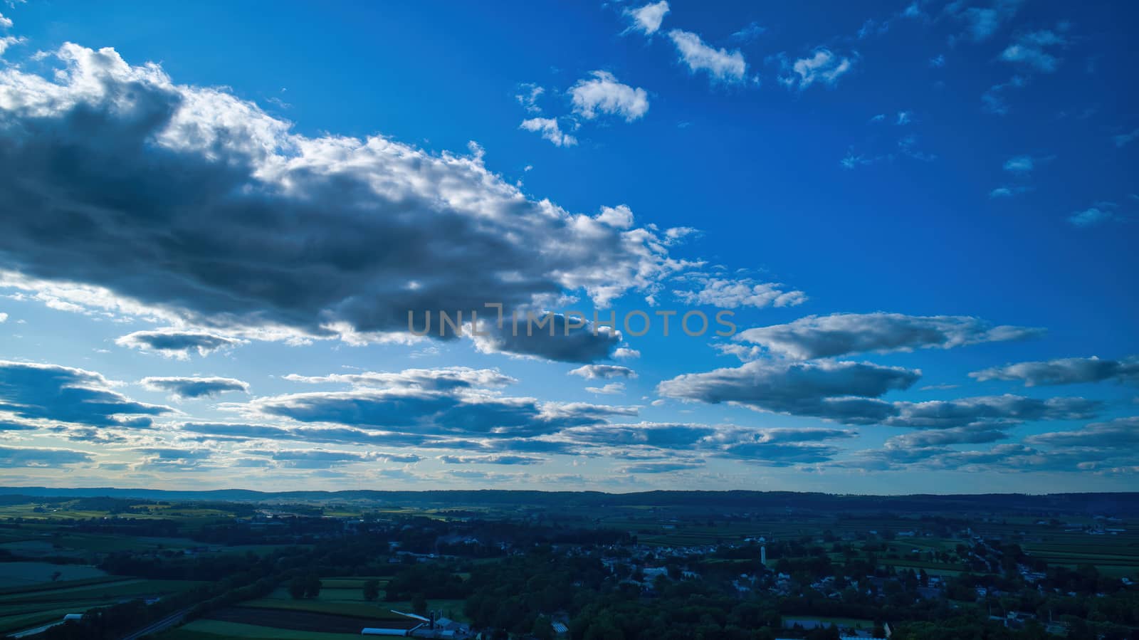 Blue sky and multiple clouds background showing a horizon and a hidden sun