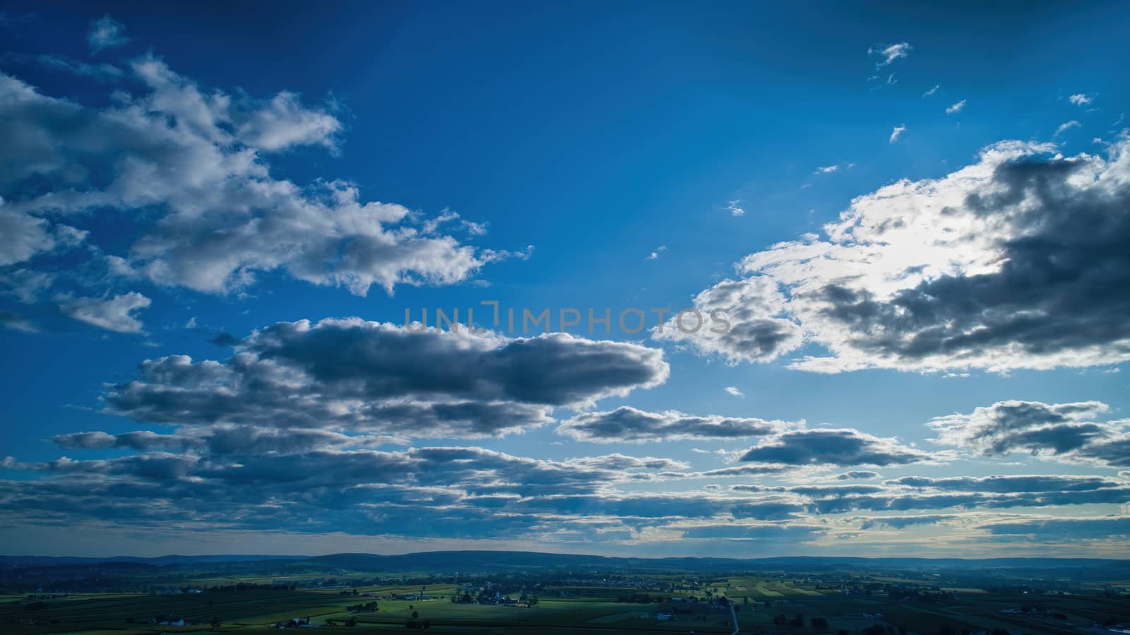 Blue sky and multiple clouds background showing a horizon and a hidden sun