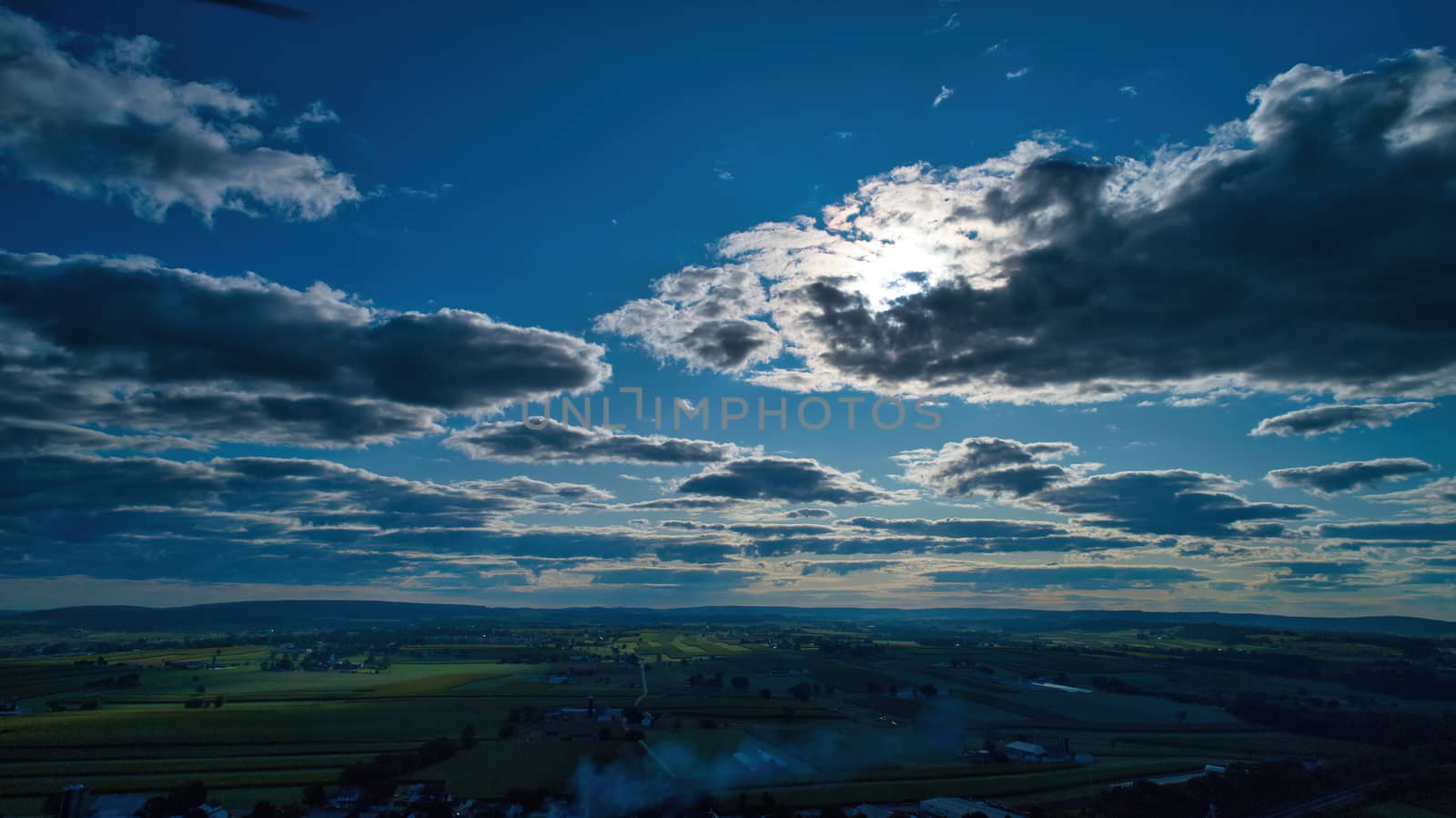Blue sky and multiple clouds background showing a horizon and a hidden sun