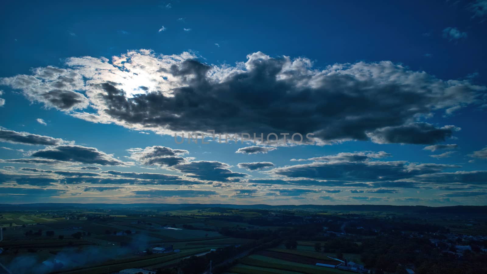 Blue sky and multiple clouds background showing a horizon and a hidden sun