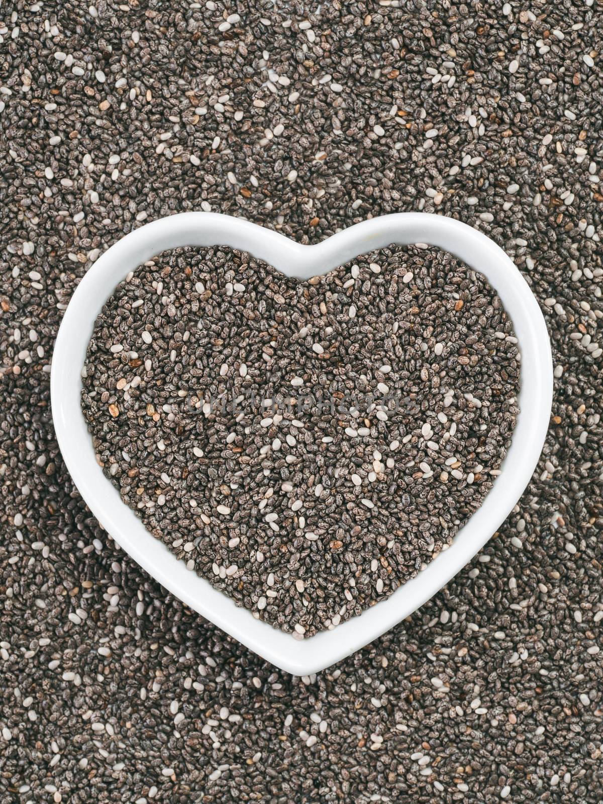 Heart-shaped bowl of chia seeds on chia background. Gluten free and healthy diet. I love chia seeds concept. Copy space.