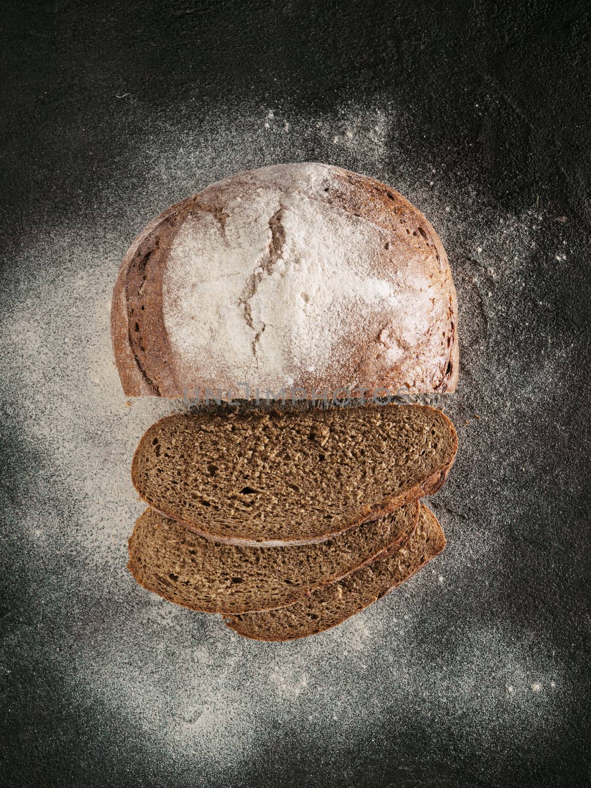 Sliced homemade sourdough rye bread with rye flour on black textured background. Top view or flat-lay. Low key