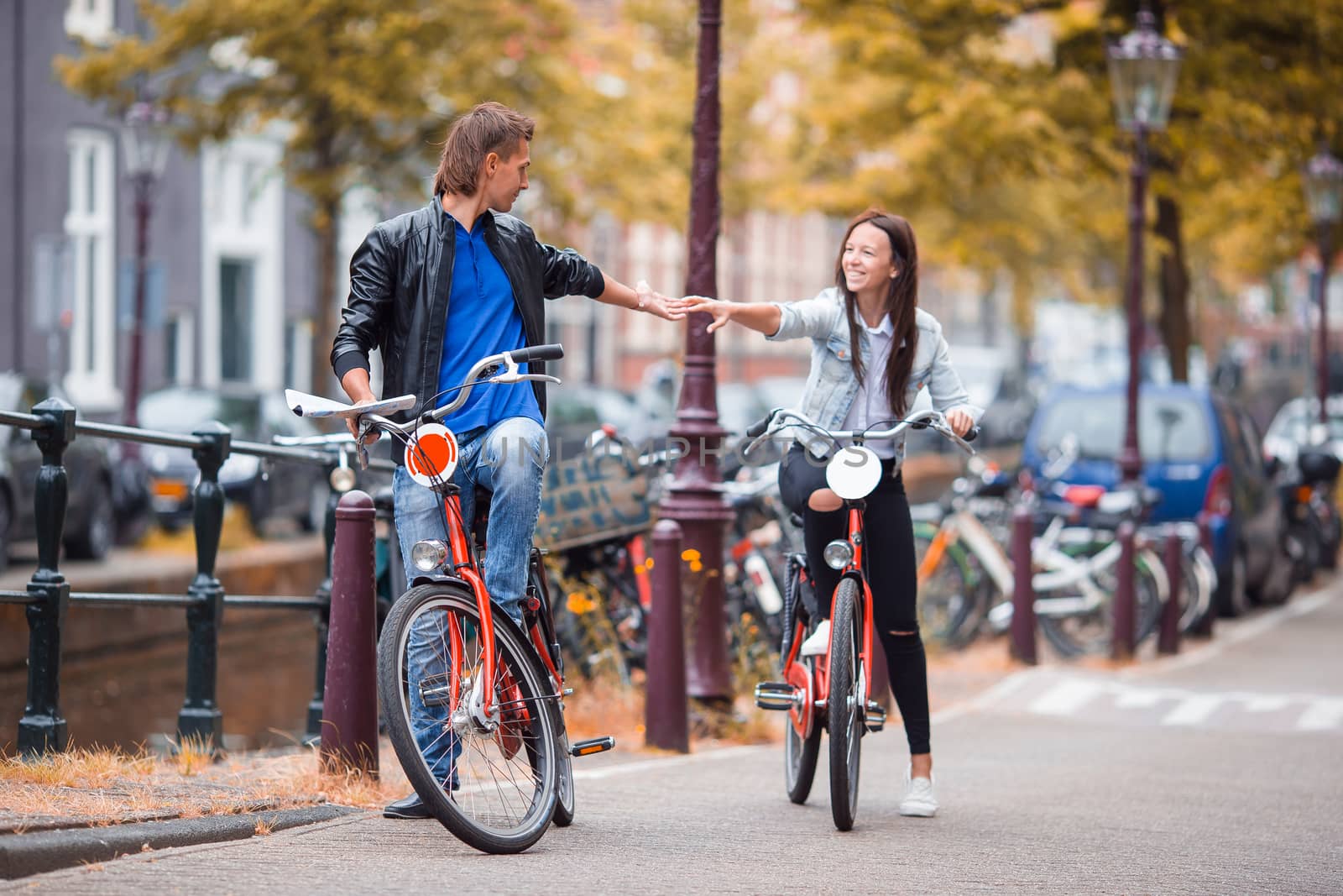 Young happy caucasian couple on bikes in old streets in Amsterdam by travnikovstudio