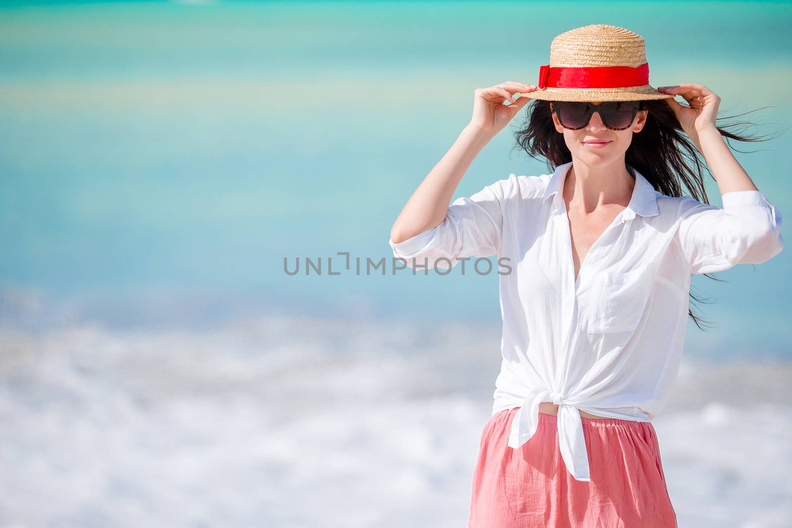 Young beautiful woman on white sand tropical beach. Caucasian girl with hat in white dress background the sea by travnikovstudio