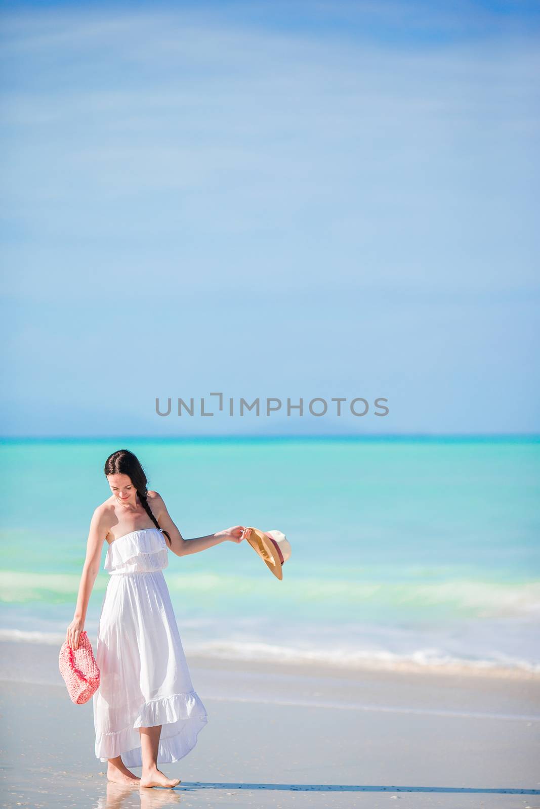 Young beautiful woman on white sand tropical beach. Caucasian girl with hat in dress background the sea by travnikovstudio