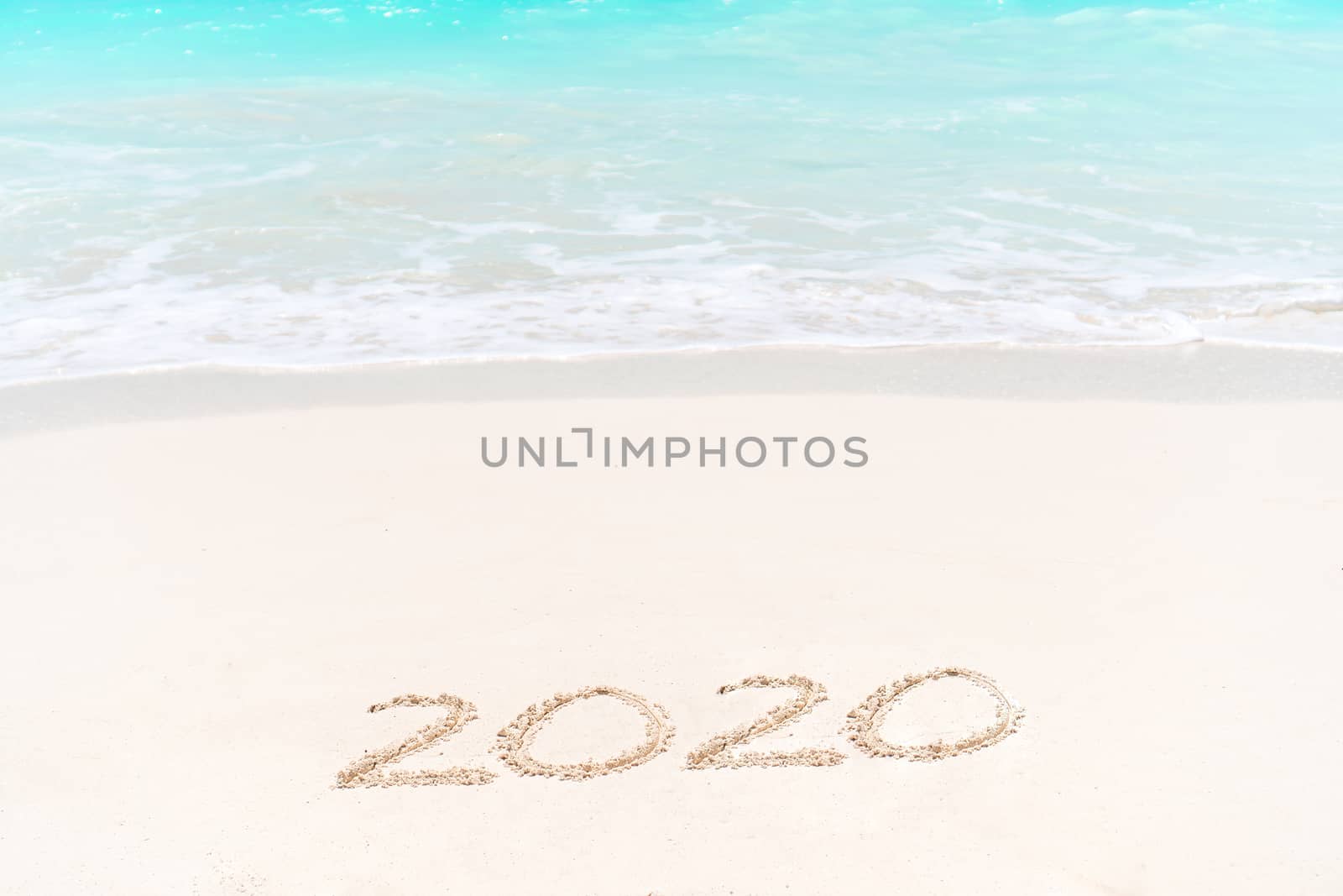 2020 handwritten on sandy beach with soft ocean wave on background by travnikovstudio