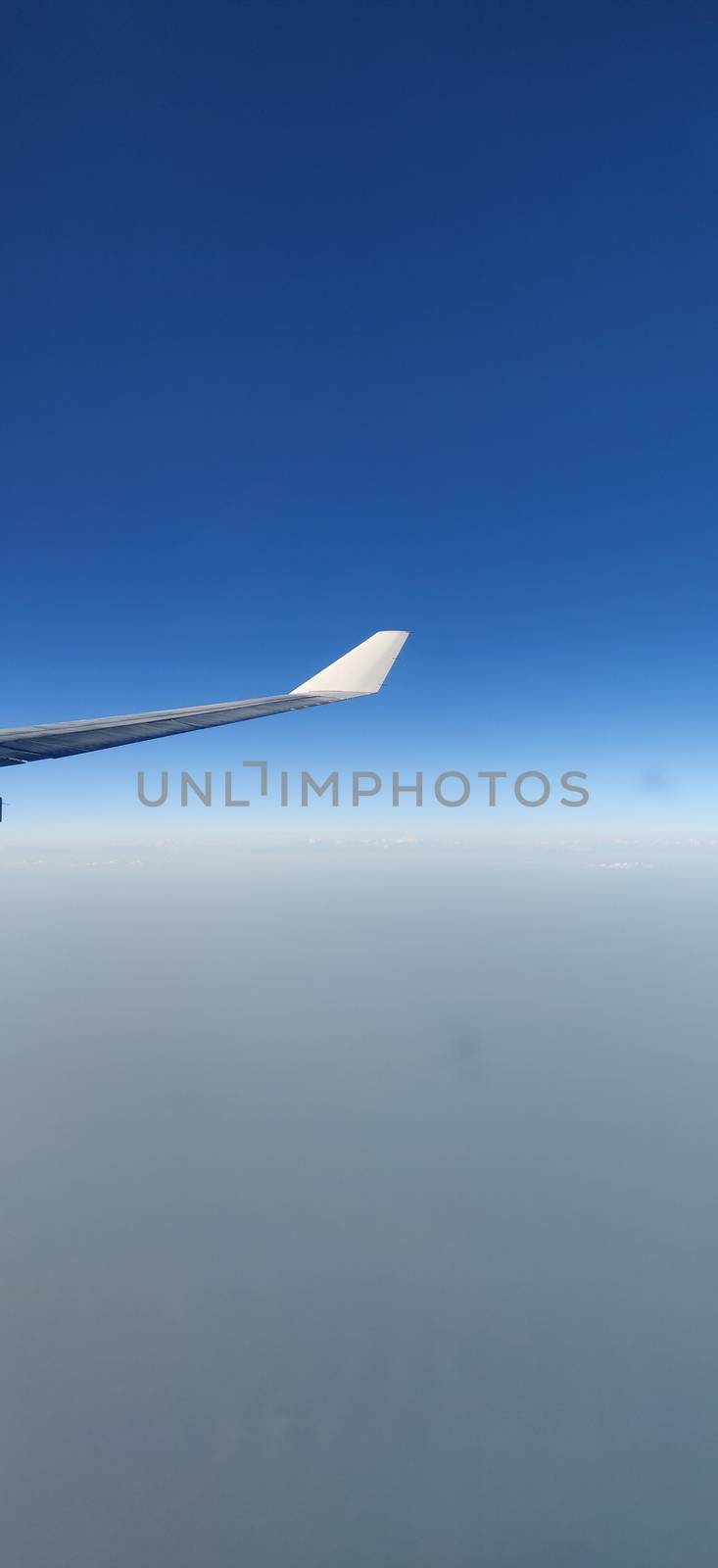 Airplane wing seen from the window of the airplane amidst blue sky and above clouds