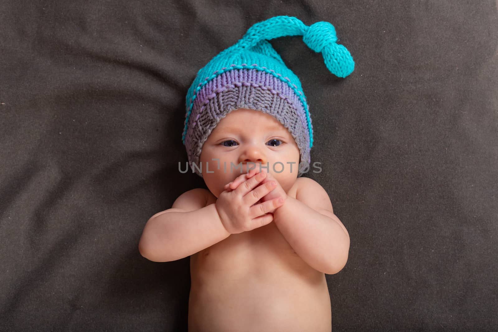 Beautiful baby girl in the studio on a dark gray background in bare pants and a winter hat.