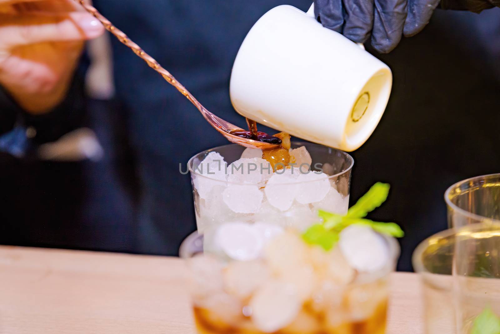 Barman making a coffee cocktail and a mojito in the foreground with his glass of ice and mint