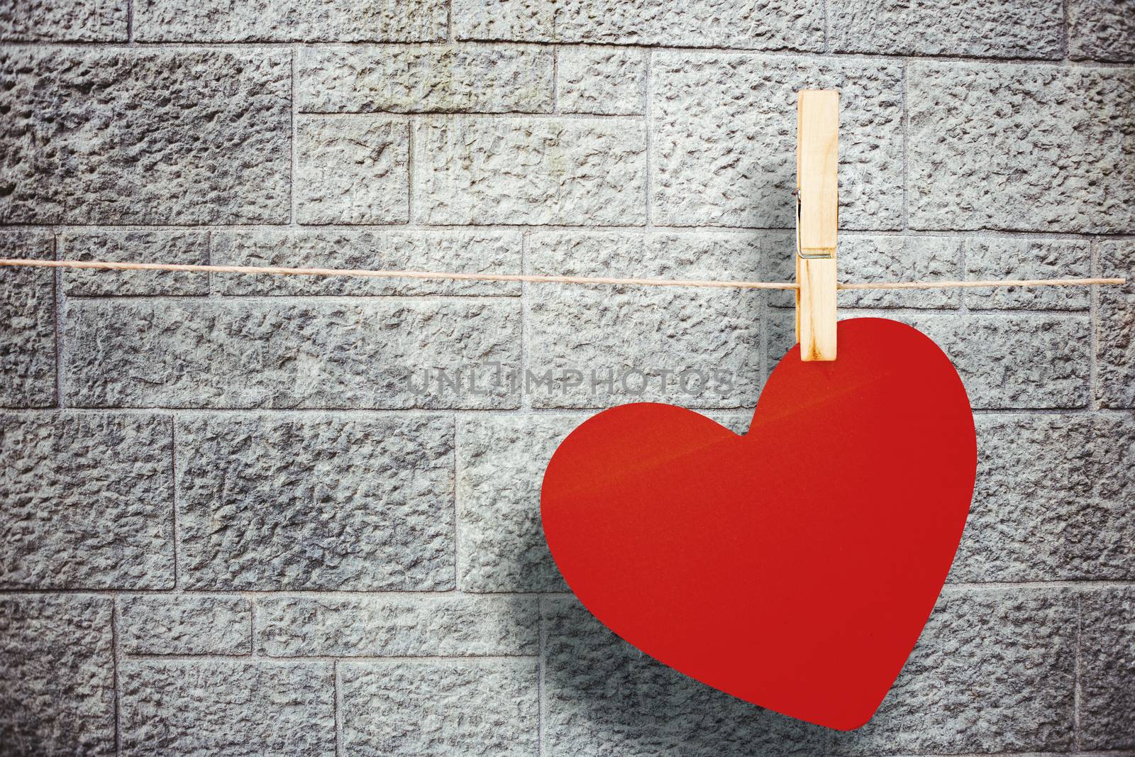 Heart hanging on line against grey brick wall