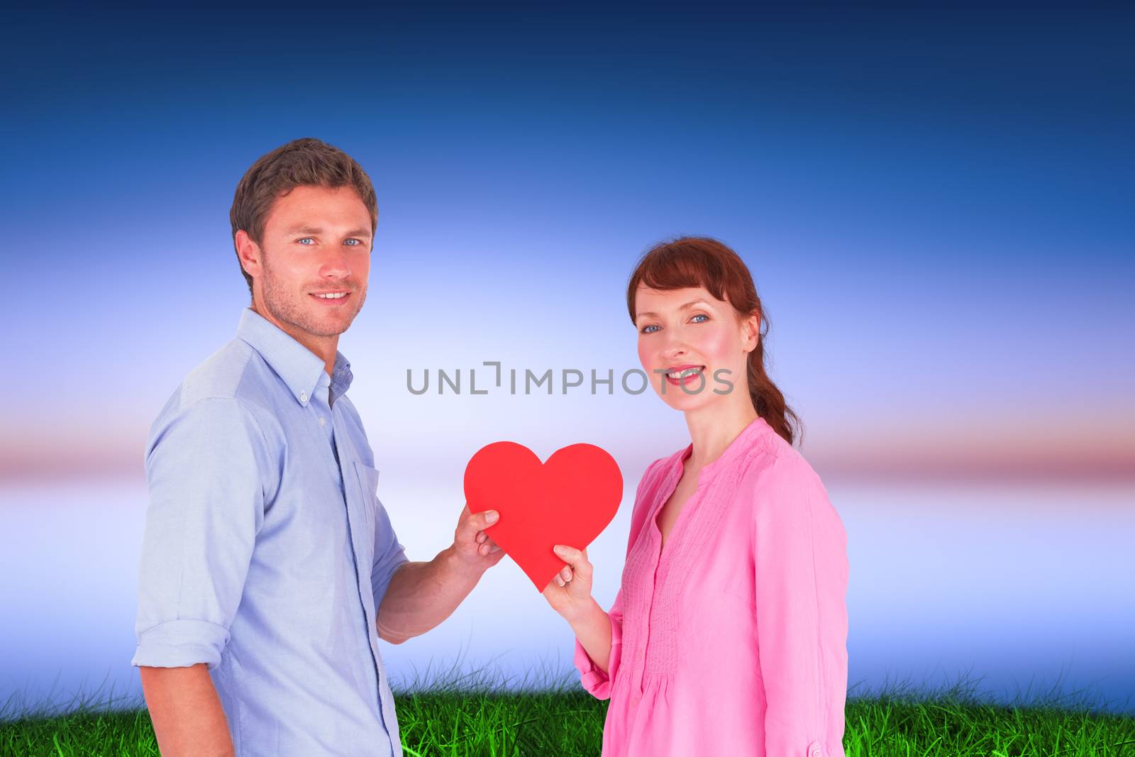 Couple holding a red heart against green grass under blue and purple sky