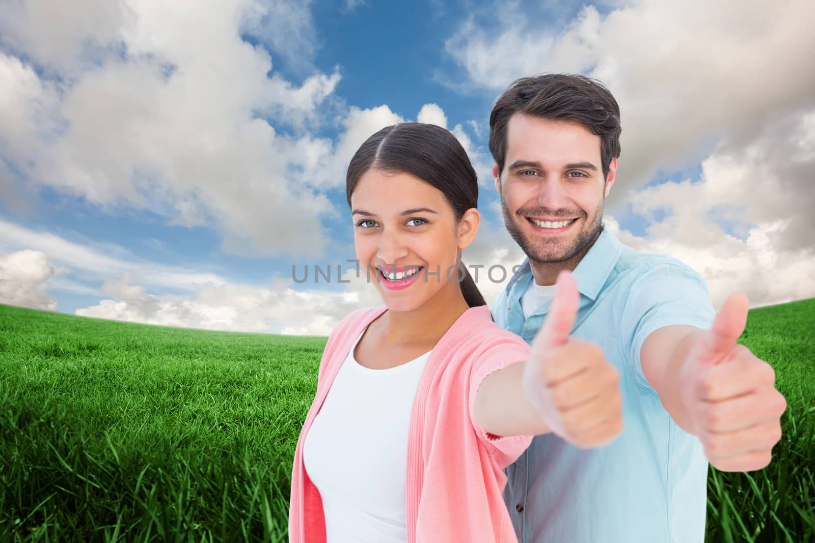 Happy couple showing thumbs up against green field under blue sky