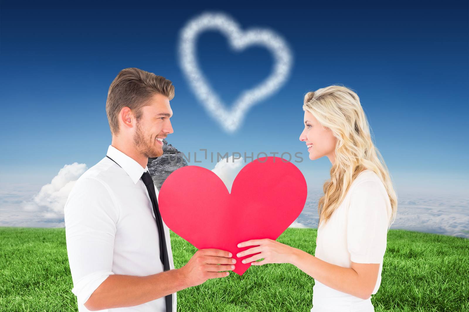Attractive young couple holding red heart against clouds over mountain peak