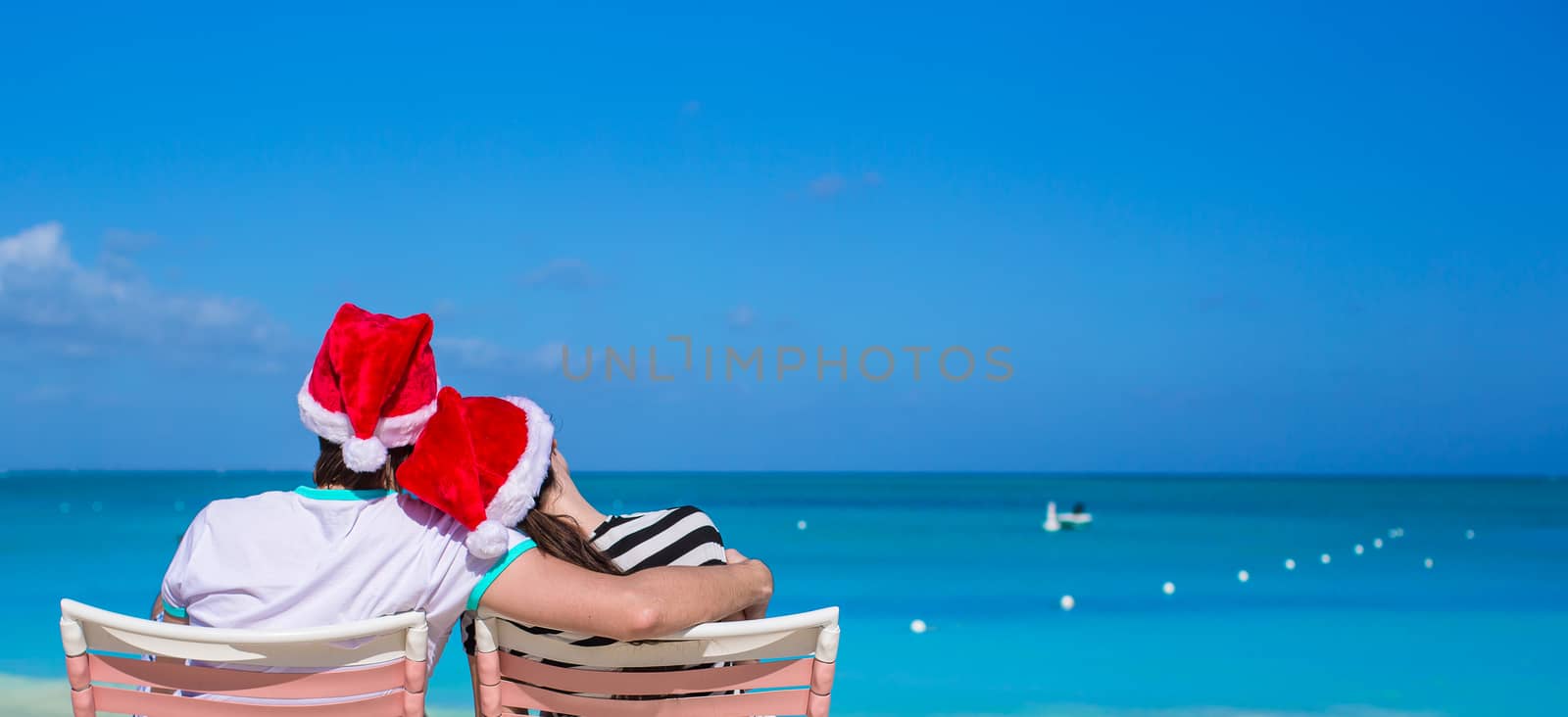 Back view of couple in Santa hats enjoy beach vacation by travnikovstudio