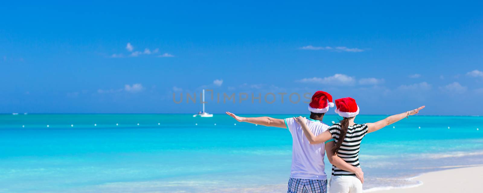 Young romantic couple in Santa hats during beach vacation by travnikovstudio