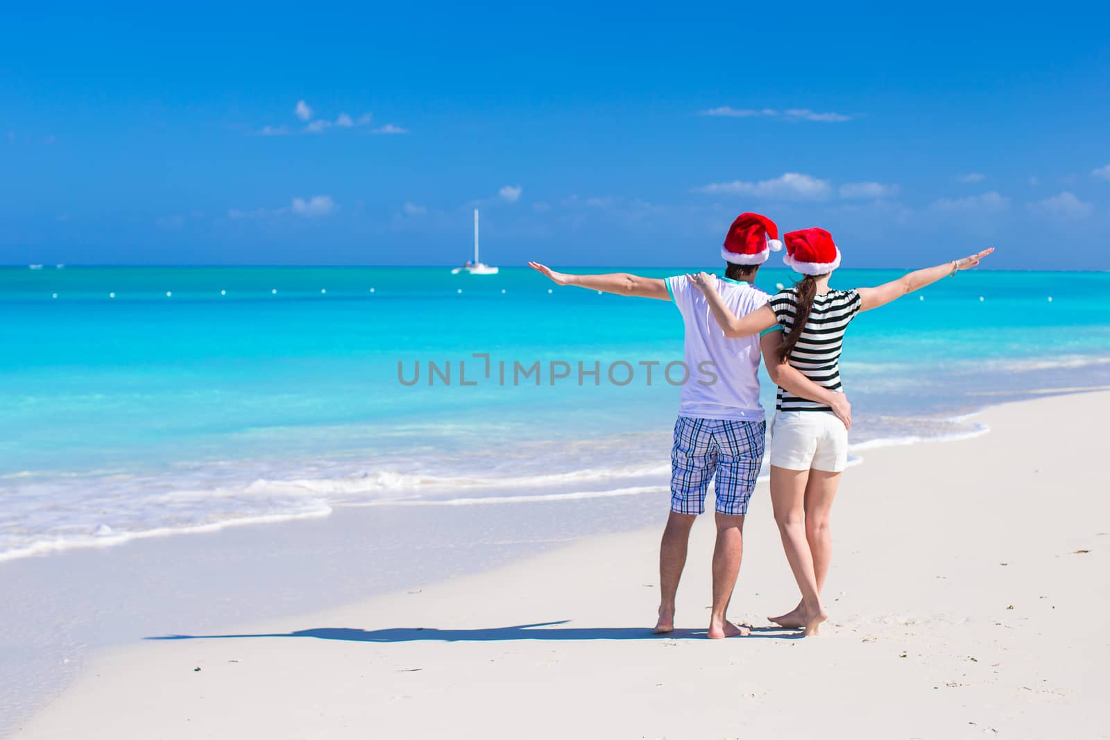 Young romantic couple in Santa hats during beach vacation by travnikovstudio