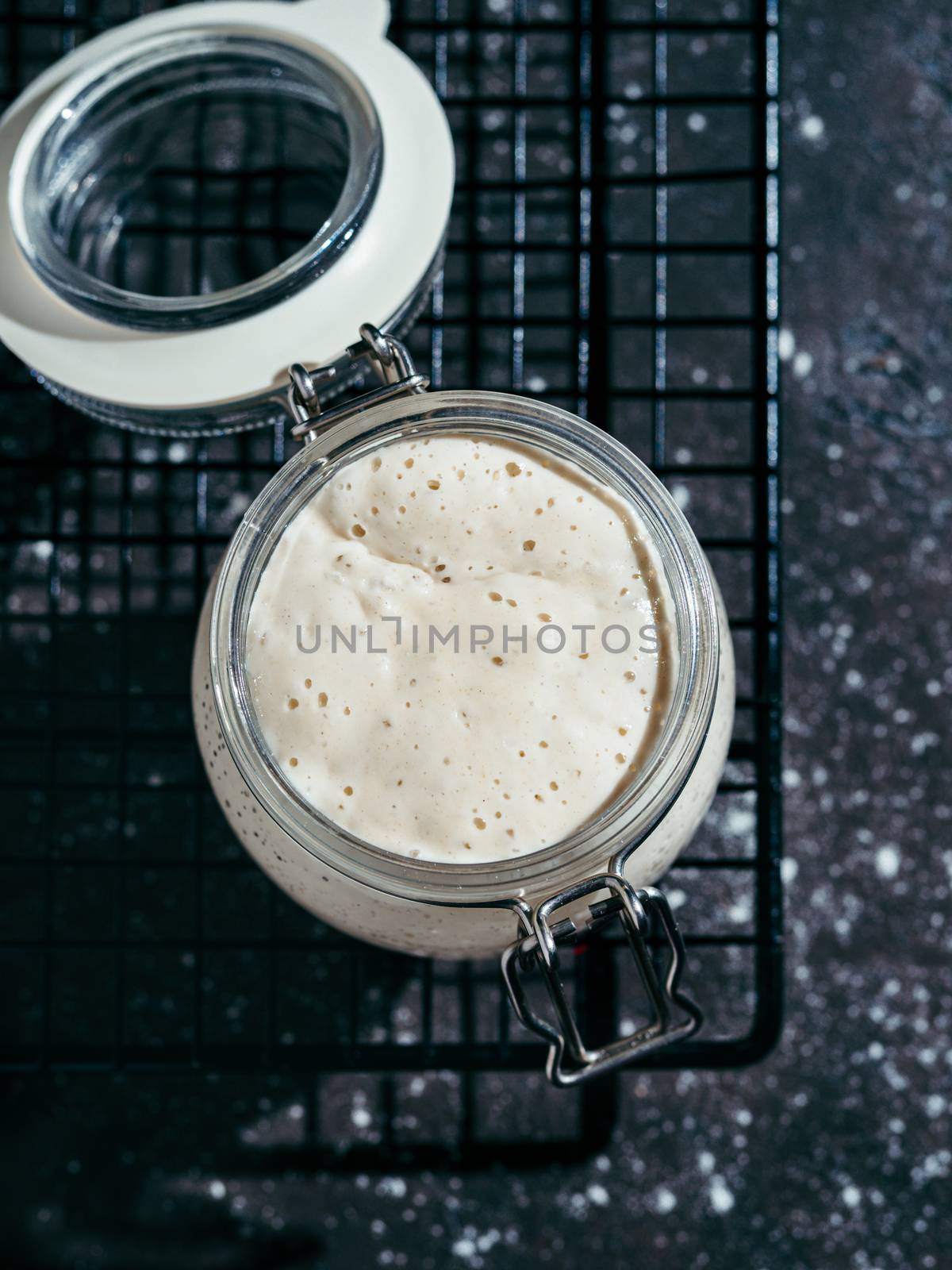 Wheat sourdough starter. Glass jar with sourdough starter on dark background, copy space. Vertical.