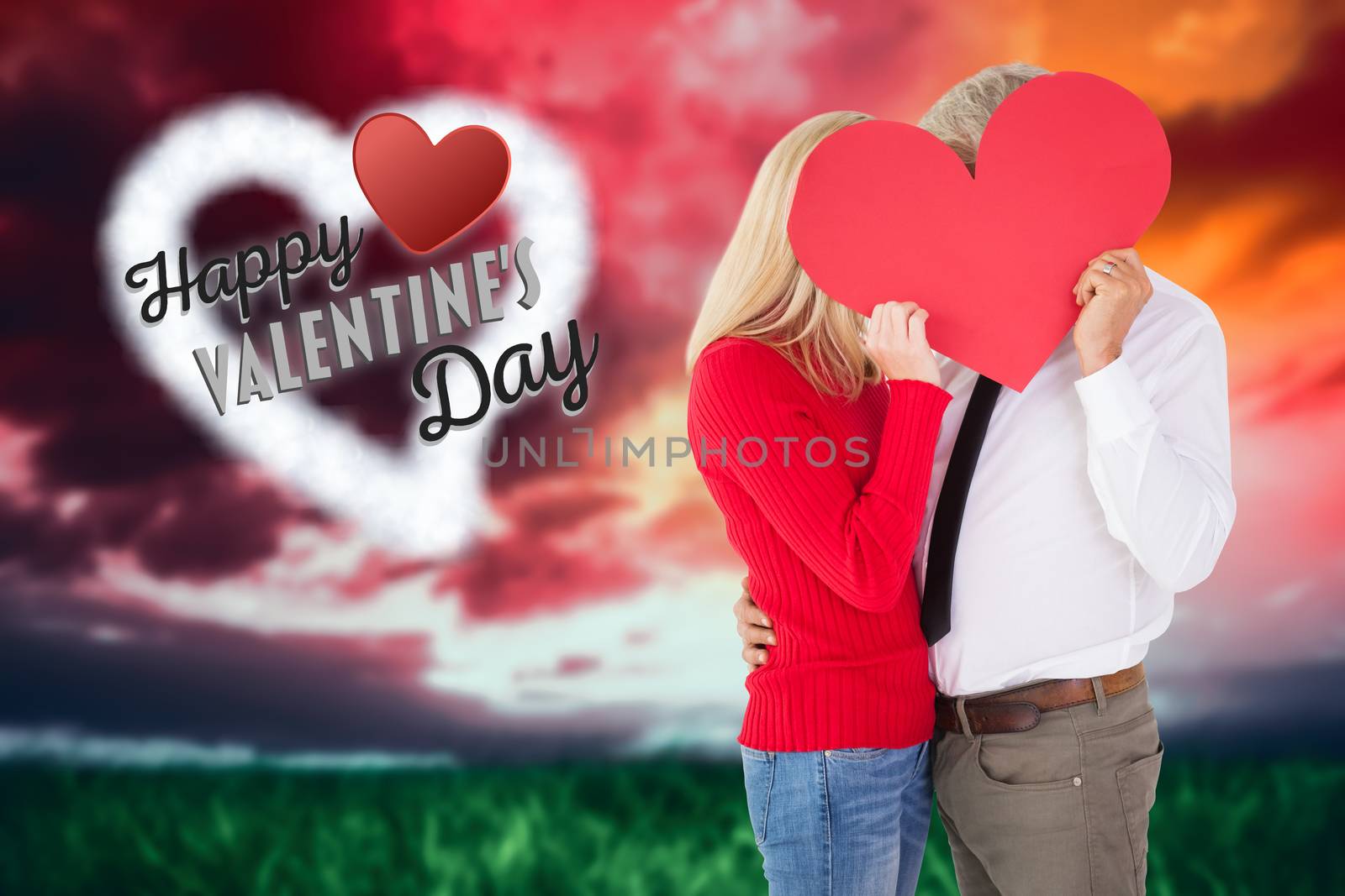 Handsome man getting a heart card form wife against green grass under red and purple sky